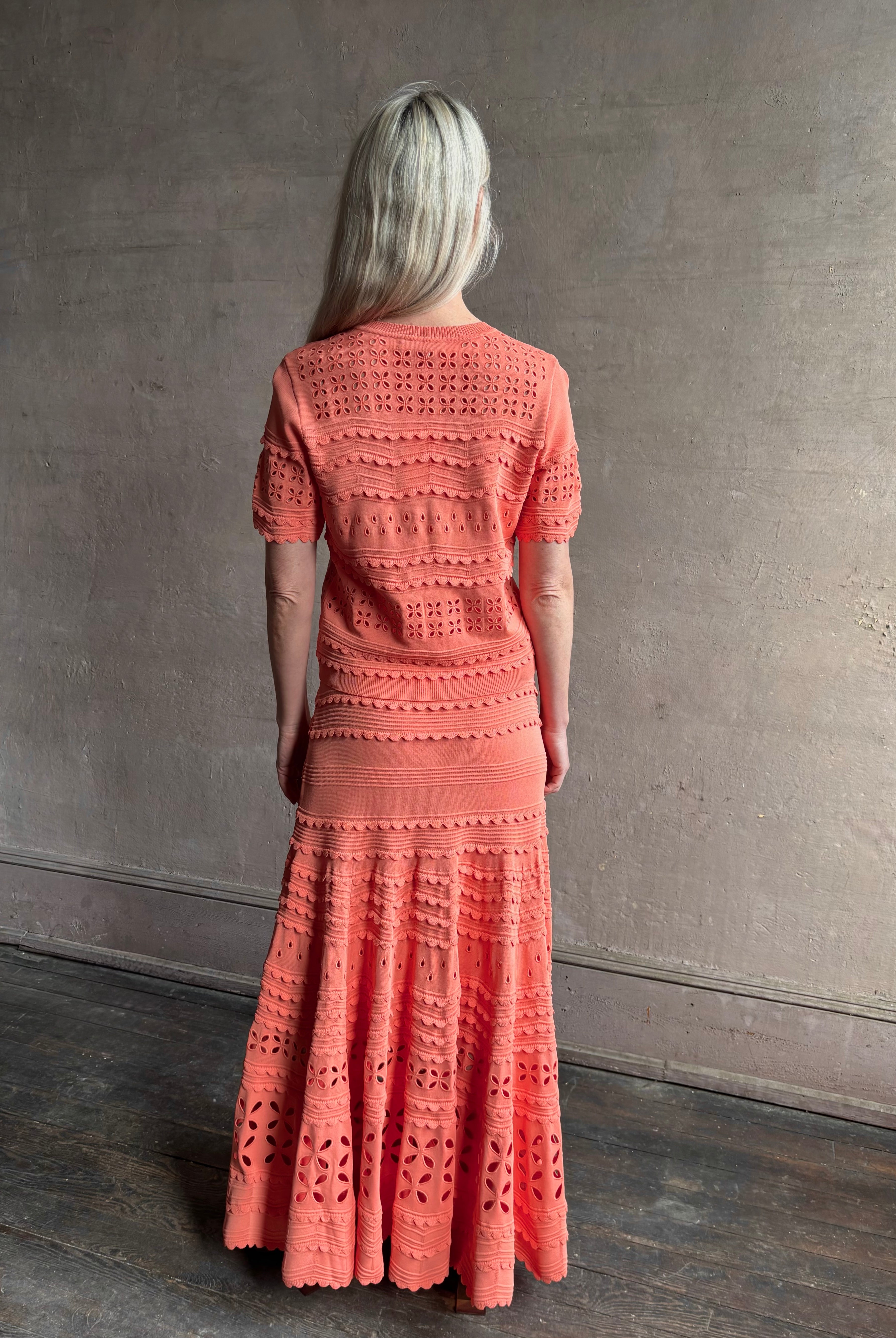 Woman wearing the romantic Abriana Eyelet Knit Cardigan from Ulla Johnson rendered in a luminous coral hue and crafted from luxury knit with round neck, button front and short sleeves