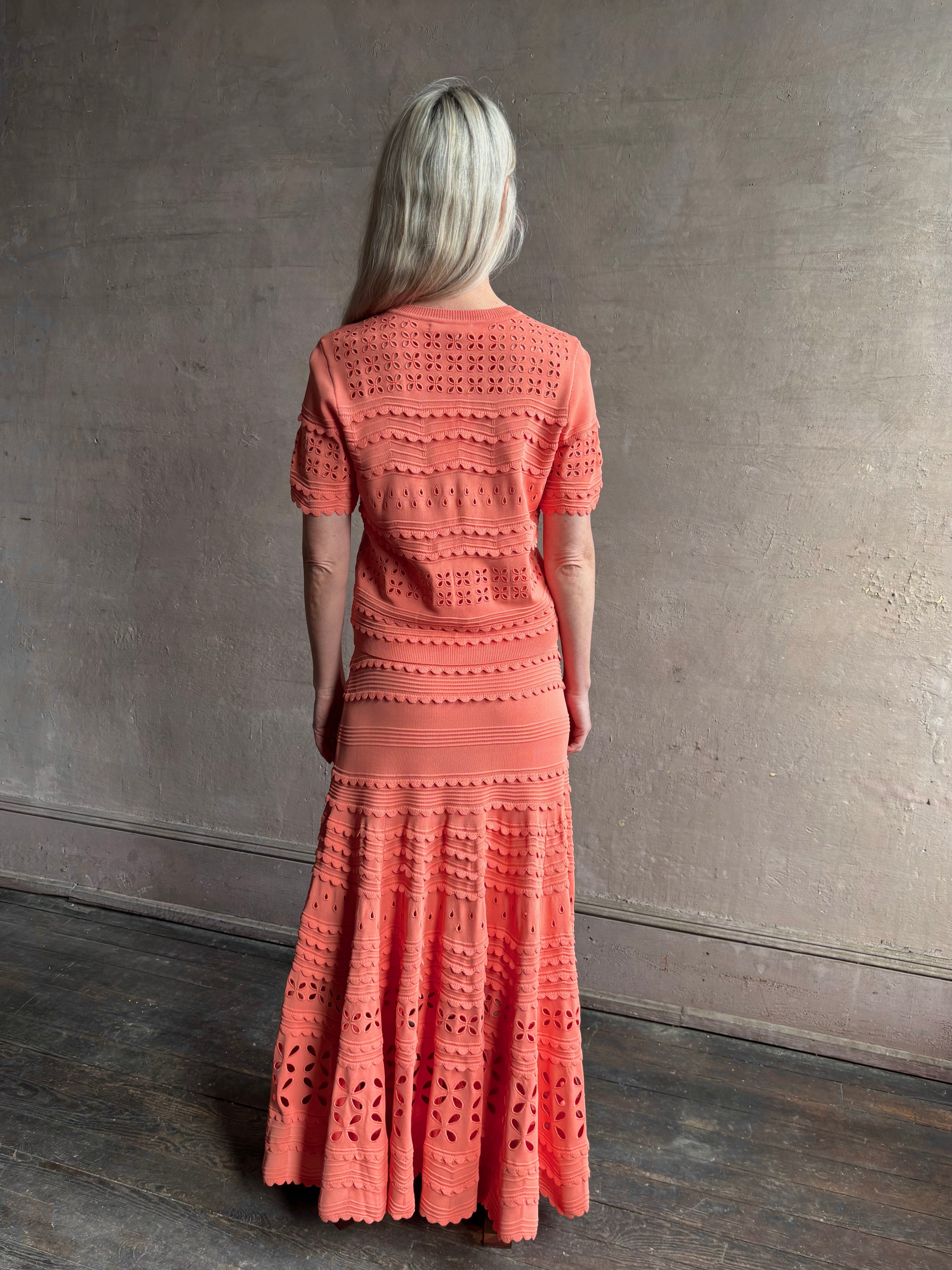 Woman wearing the romantic Abriana Eyelet Knit Cardigan from Ulla Johnson rendered in a luminous coral hue and crafted from luxury knit with round neck, button front and short sleeves