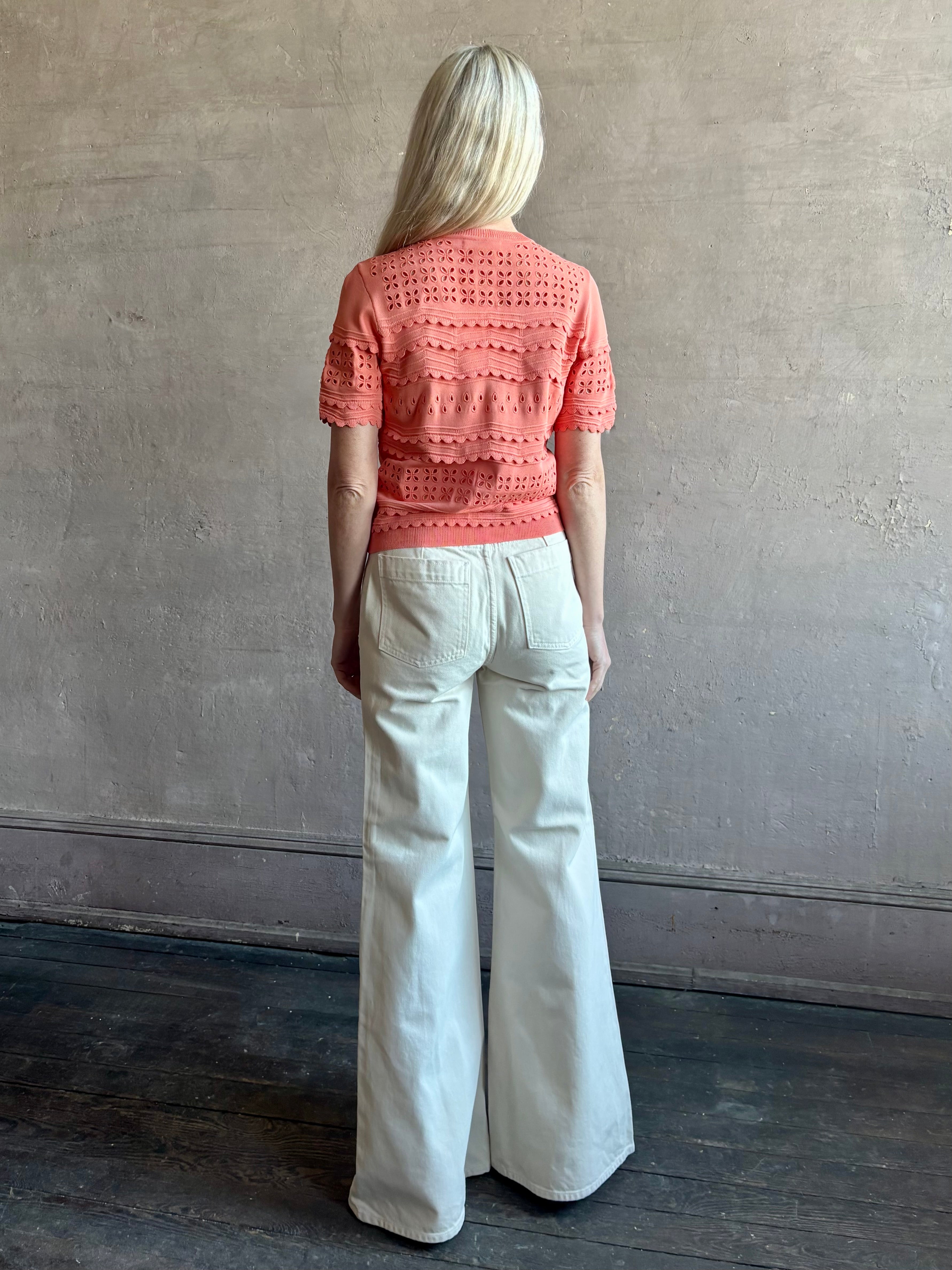 Woman wearing the romantic Abriana Eyelet Knit Cardigan from Ulla Johnson rendered in a luminous coral hue and crafted from luxury knit with round neck, button front and short sleeves