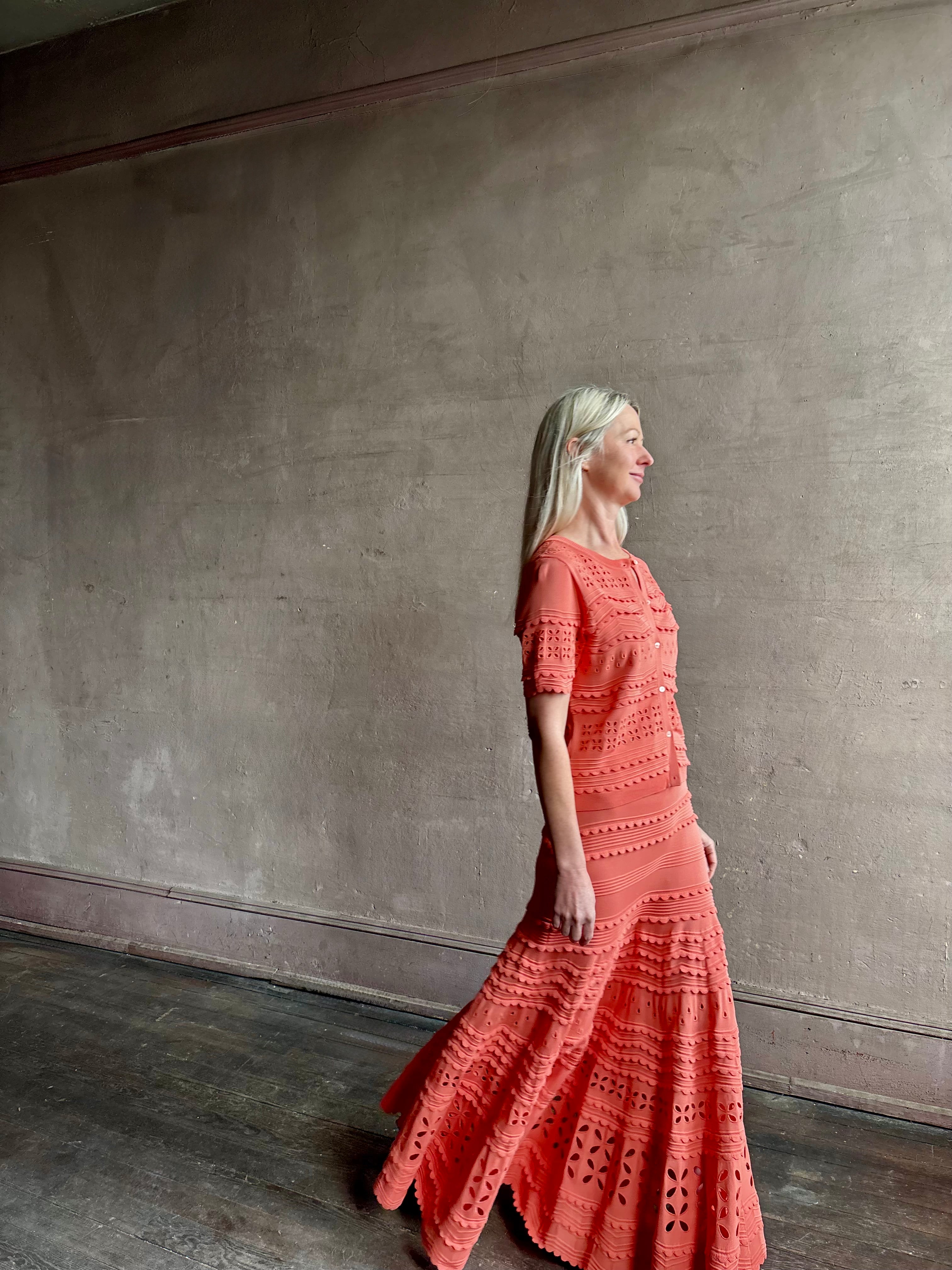 Woman wearing the feminine Annisa Eyelet Knit A-line maxi skirt from Ulla Johnson rendered in a luminous coral hue and crafted from luxury knit with matching top