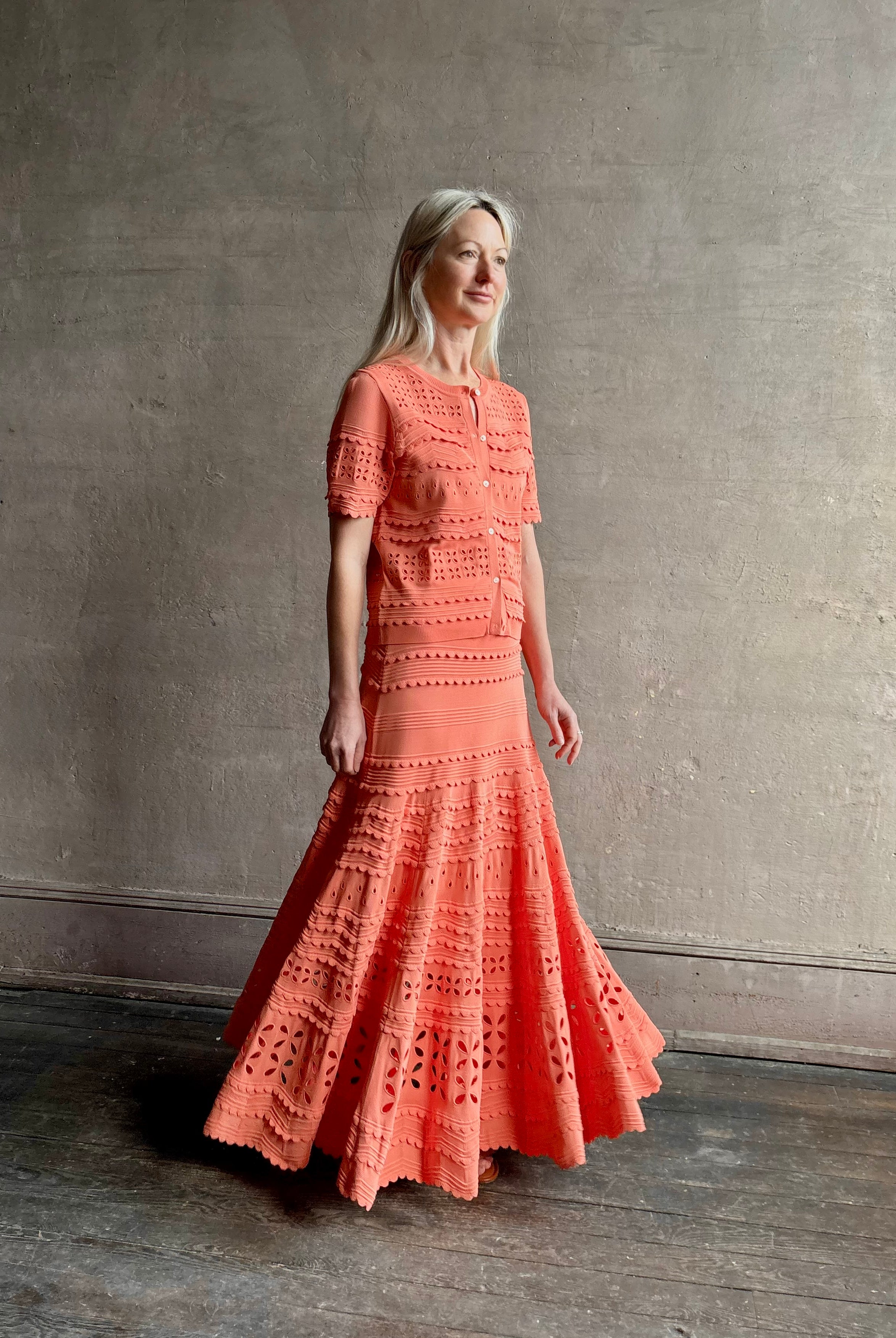 Woman wearing the feminine Annisa Eyelet Knit A-line maxi skirt from Ulla Johnson rendered in a luminous coral hue and crafted from luxury knit with matching top