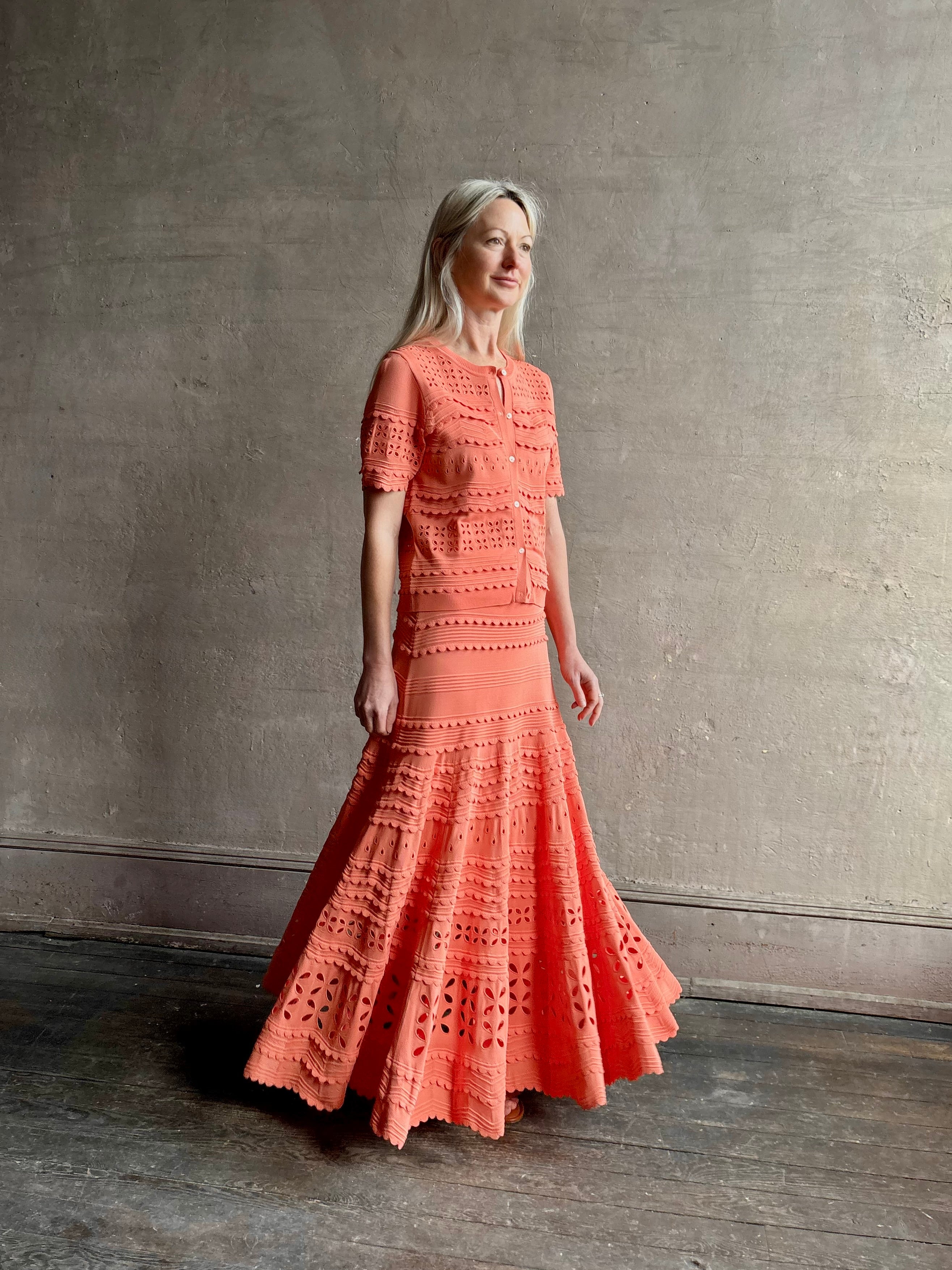 Woman wearing the feminine Annisa Eyelet Knit A-line maxi skirt from Ulla Johnson rendered in a luminous coral hue and crafted from luxury knit with matching top