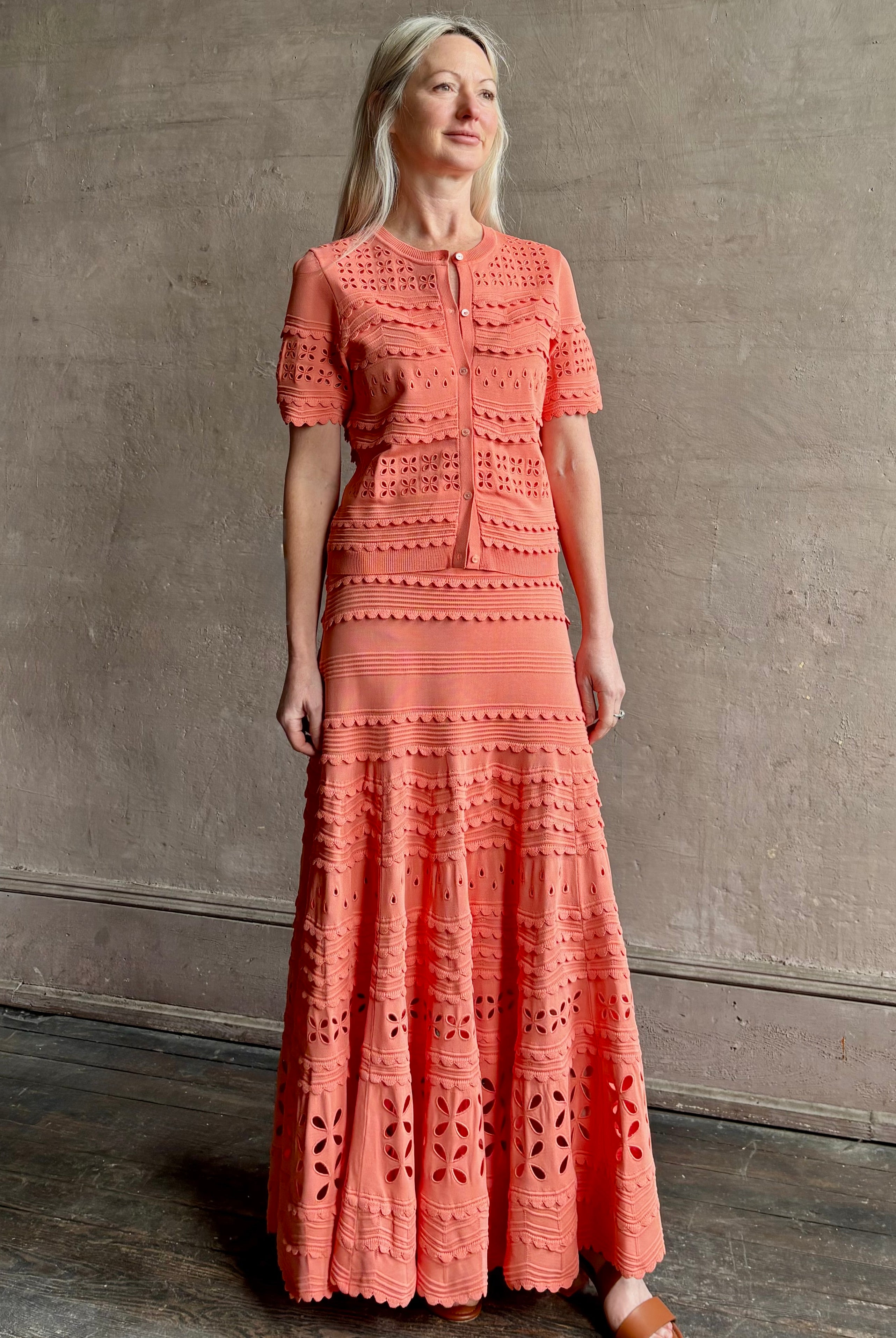 Woman wearing the feminine Annisa Eyelet Knit A-line maxi skirt from Ulla Johnson rendered in a luminous coral hue and crafted from luxury knit with matching top