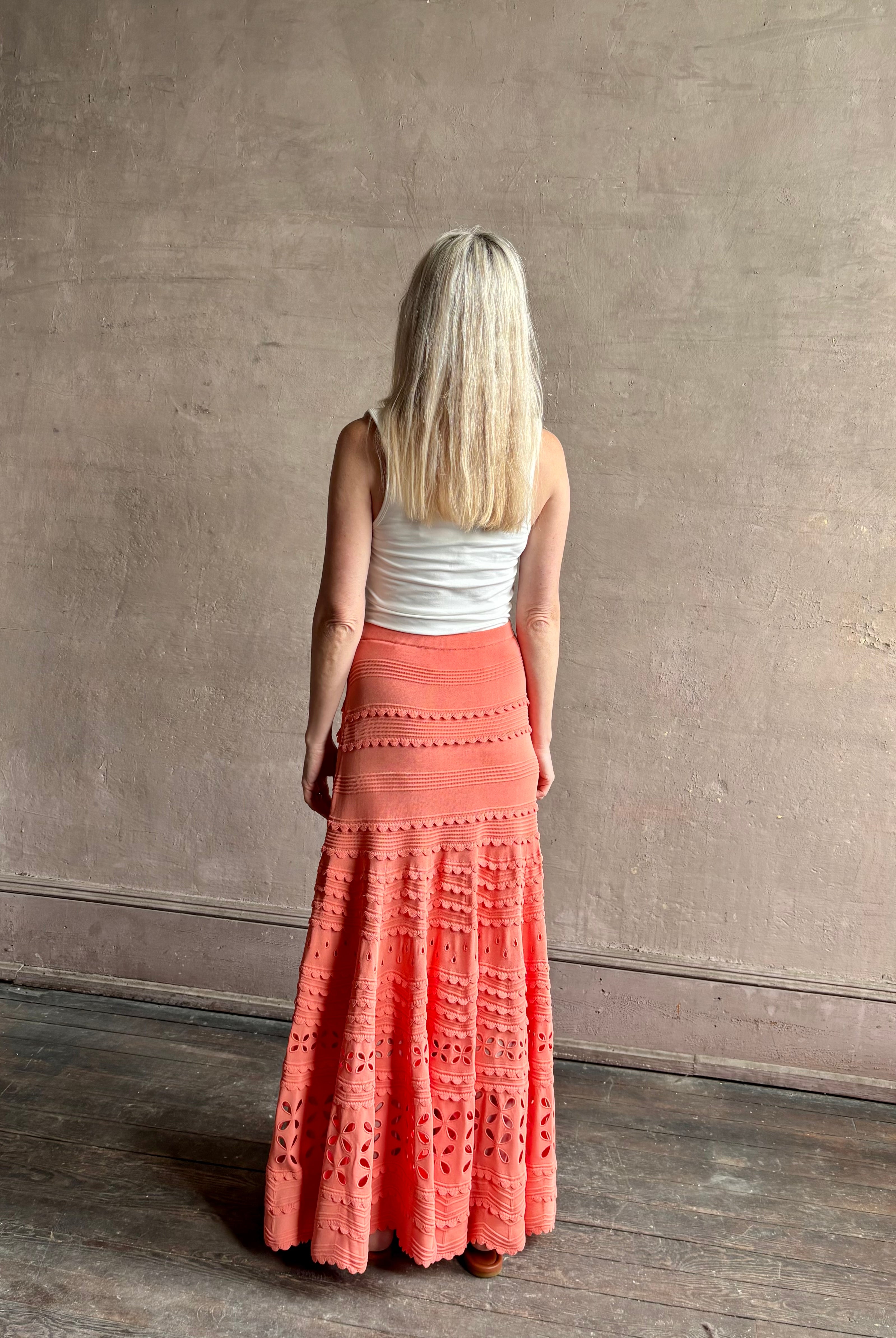 Woman wearing the feminine Annisa Eyelet Knit A-line maxi skirt from Ulla Johnson rendered in a luminous coral hue and crafted from luxury knit