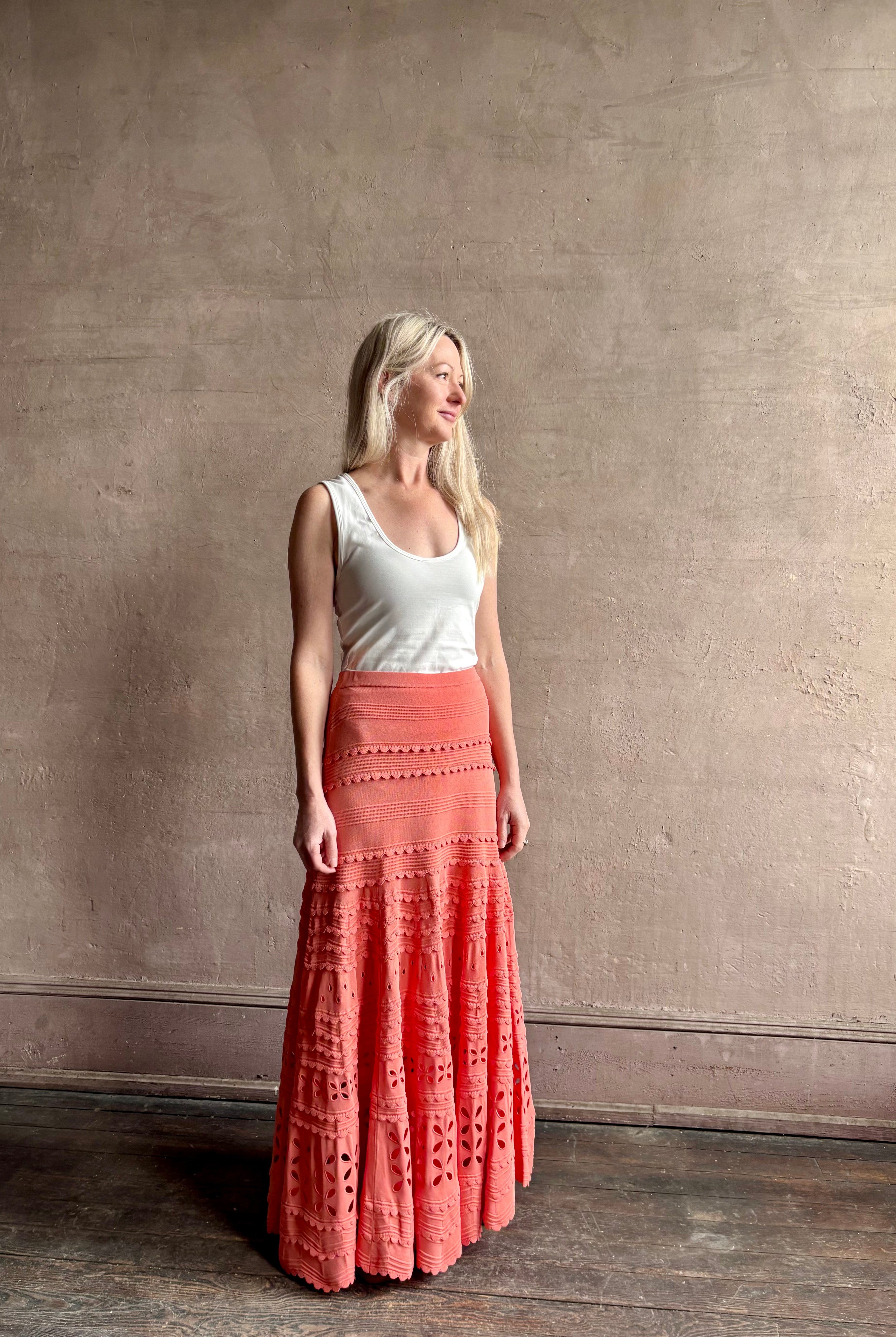 Woman wearing the feminine Annisa Eyelet Knit A-line maxi skirt from Ulla Johnson rendered in a luminous coral hue and crafted from luxury knit