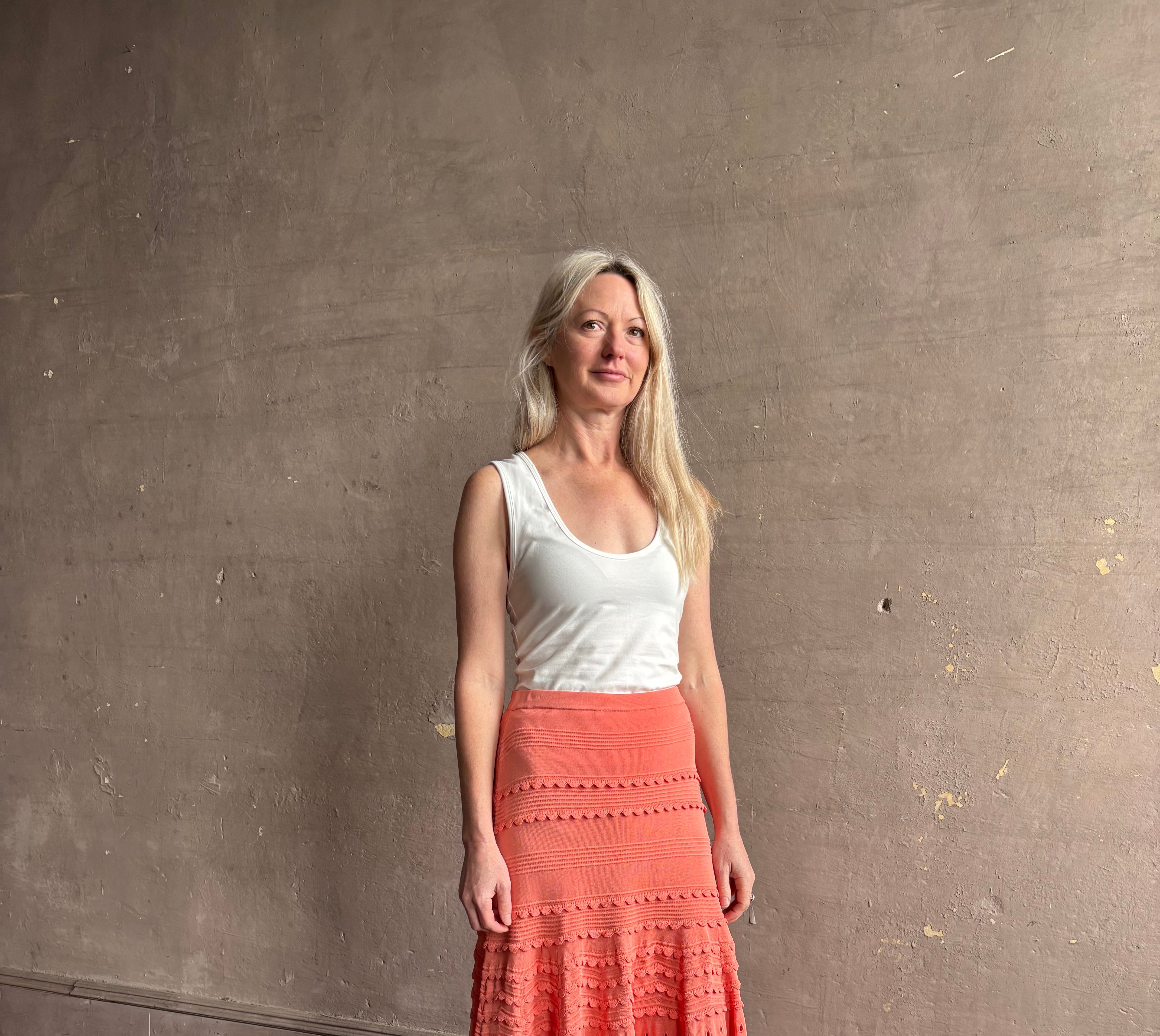 Woman wearing the feminine Annisa Eyelet Knit A-line maxi skirt from Ulla Johnson rendered in a luminous coral hue and crafted from luxury knit