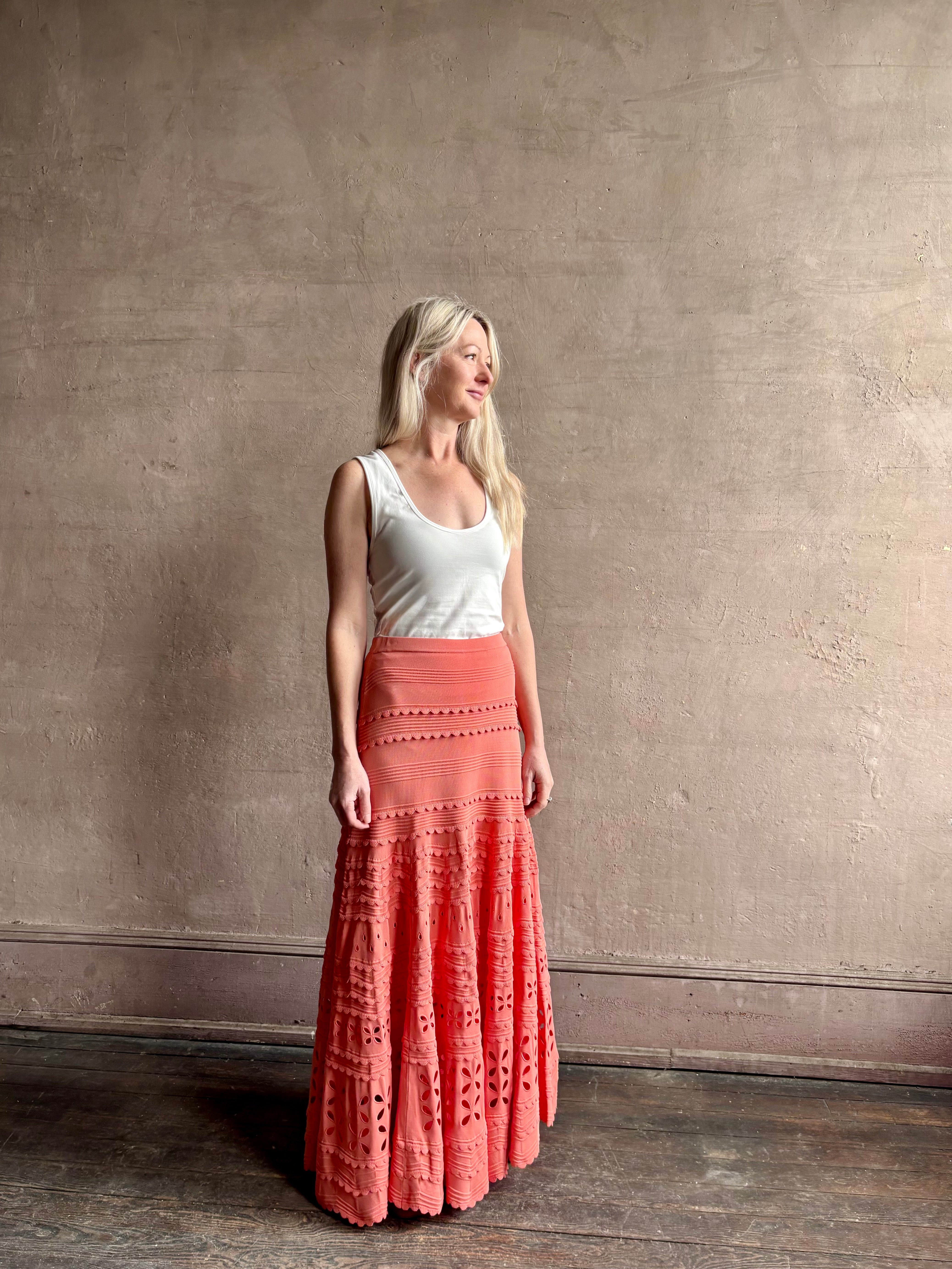 Woman wearing the feminine Annisa Eyelet Knit A-line maxi skirt from Ulla Johnson rendered in a luminous coral hue and crafted from luxury knit with matching top