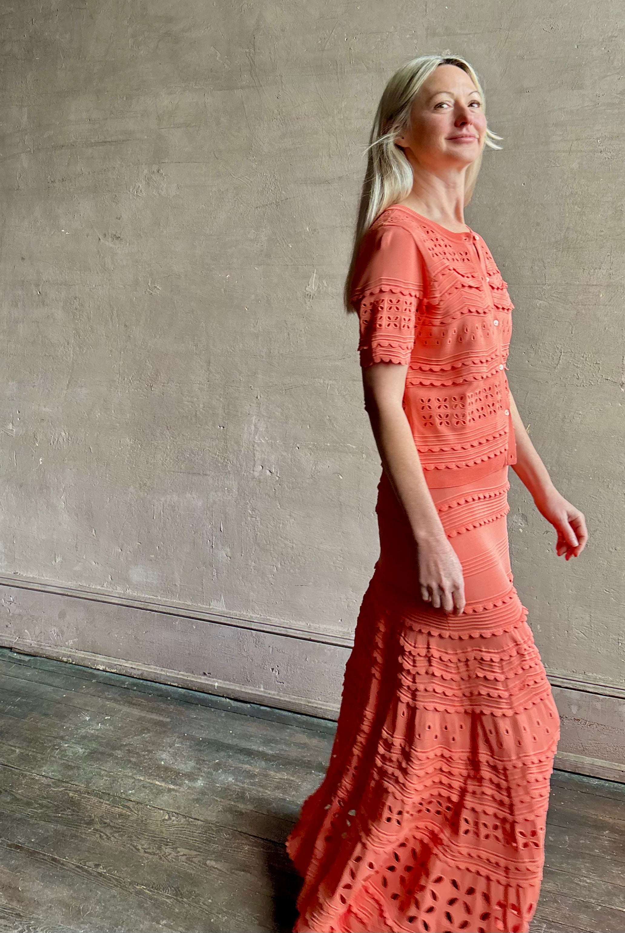 Woman wearing the feminine Annisa Eyelet Knit A-line maxi skirt from Ulla Johnson rendered in a luminous coral hue and crafted from luxury knit with matching top