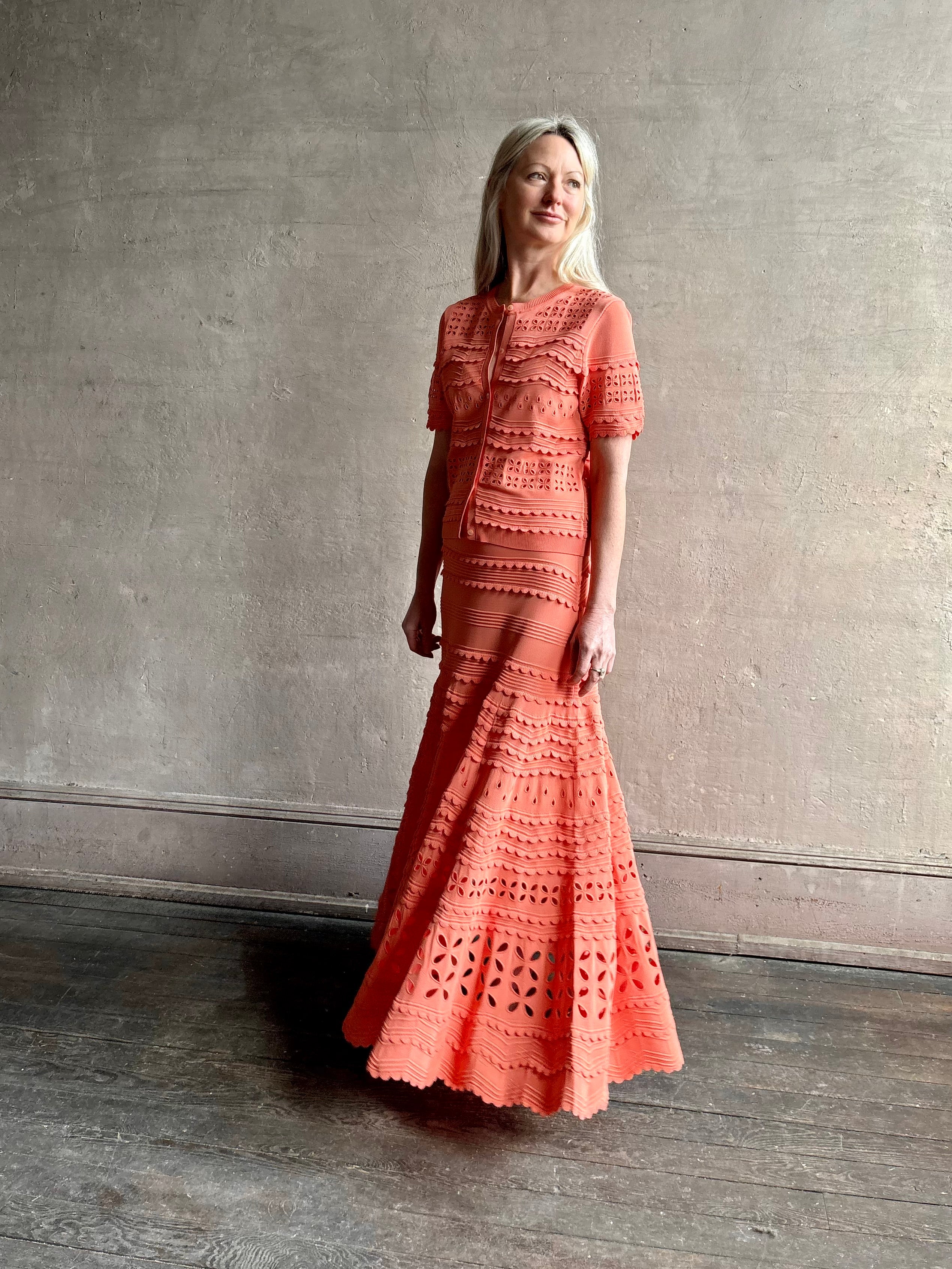 Woman wearing the feminine Annisa Eyelet Knit A-line maxi skirt from Ulla Johnson rendered in a luminous coral hue and crafted from luxury knit with matching top