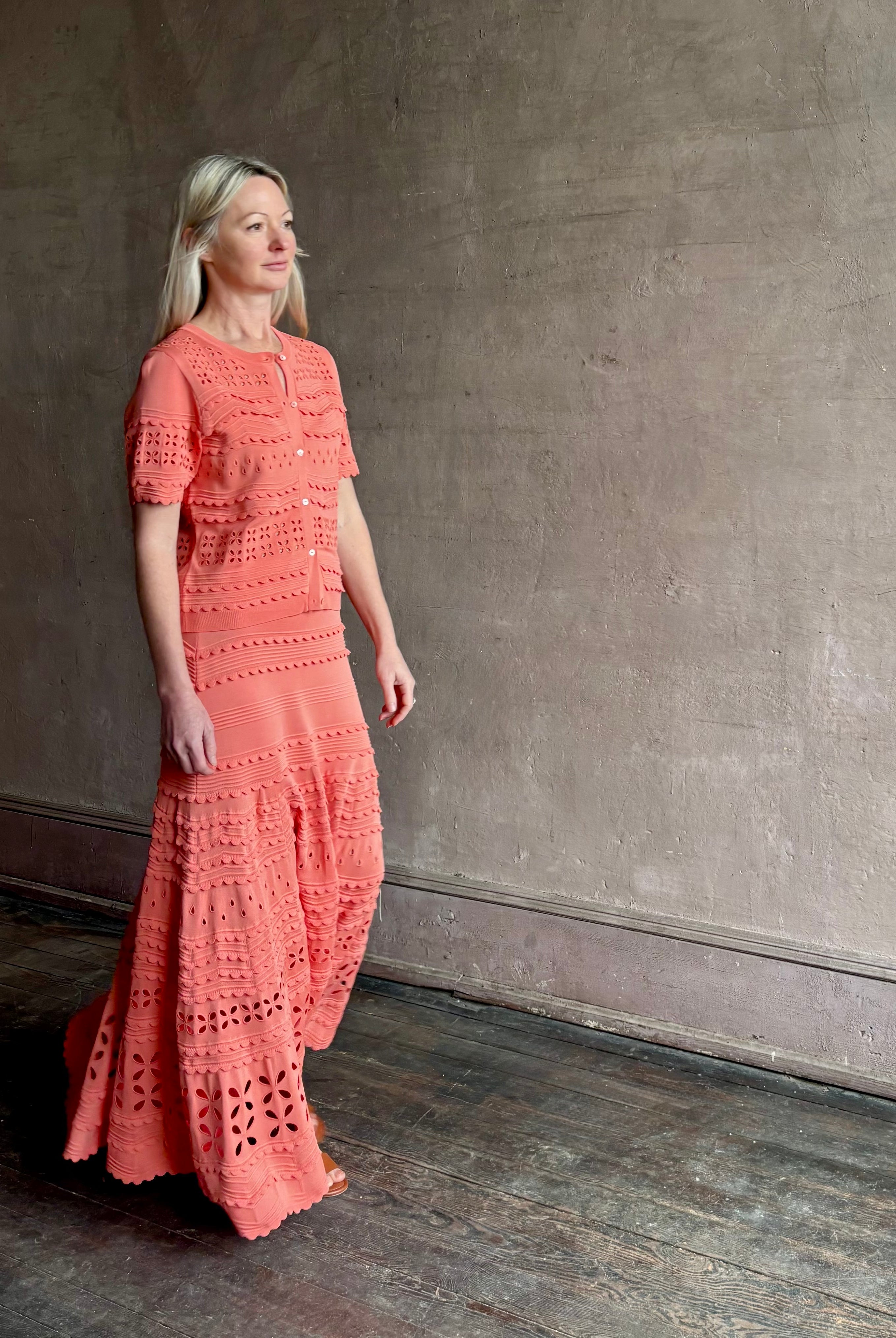 Woman wearing the feminine Annisa Eyelet Knit A-line maxi skirt from Ulla Johnson rendered in a luminous coral hue and crafted from luxury knit with matching top