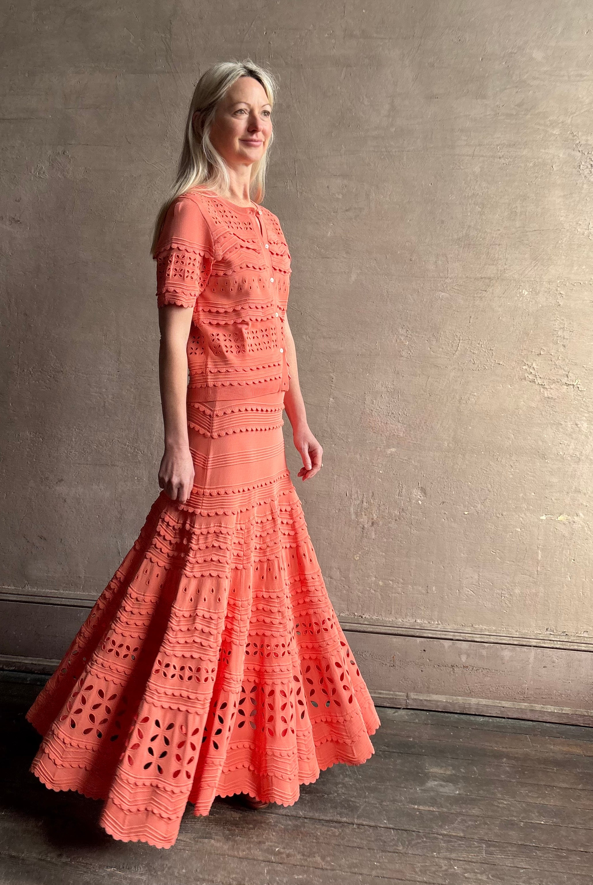 Woman wearing the feminine Annisa Eyelet Knit A-line maxi skirt from Ulla Johnson rendered in a luminous coral hue and crafted from luxury knit with matching top
