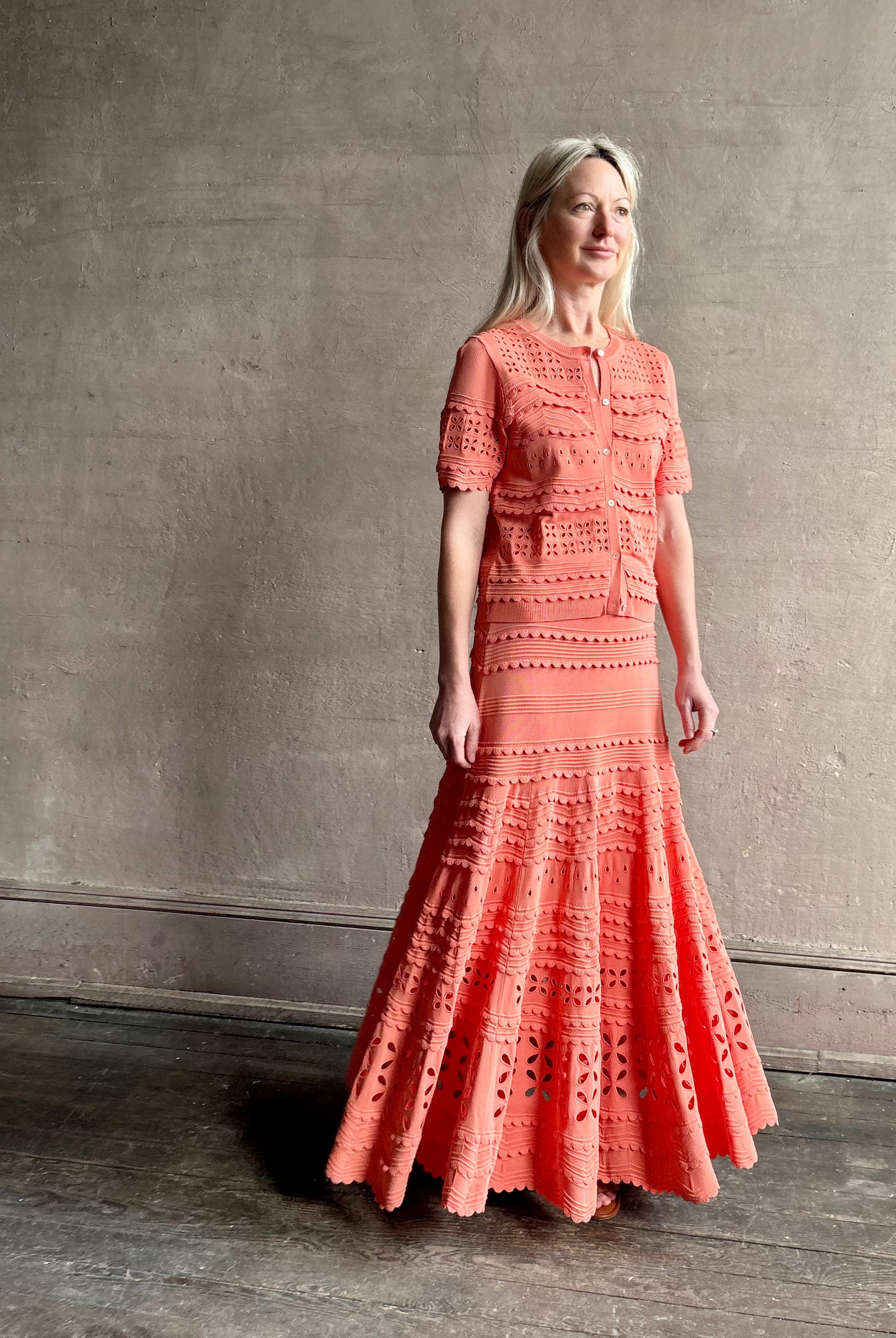 Woman wearing the feminine Annisa Eyelet Knit A-line maxi skirt from Ulla Johnson rendered in a luminous coral hue and crafted from luxury knit with matching top