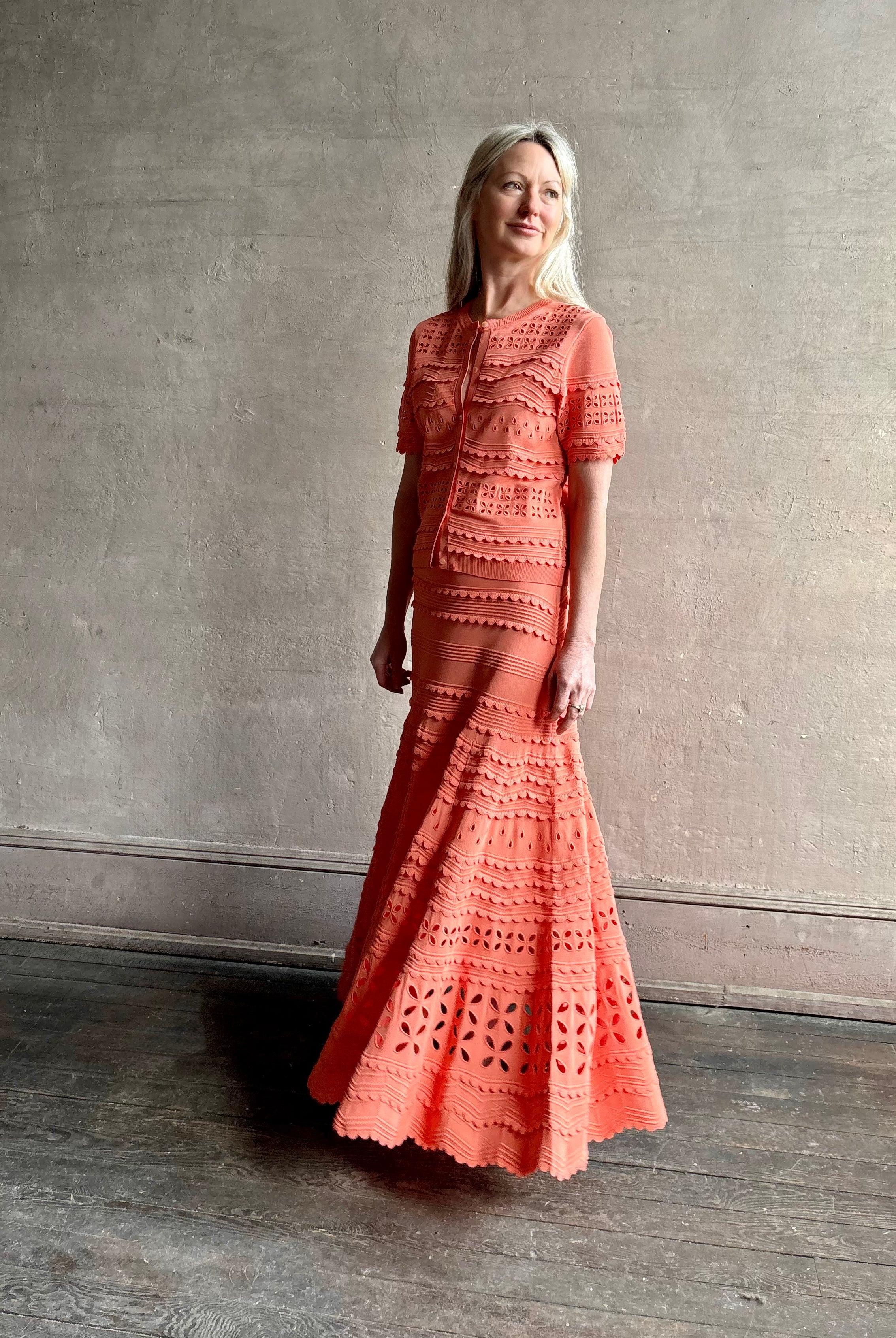 Woman wearing the feminine Annisa Eyelet Knit A-line maxi skirt from Ulla Johnson rendered in a luminous coral hue and crafted from luxury knit with matching top