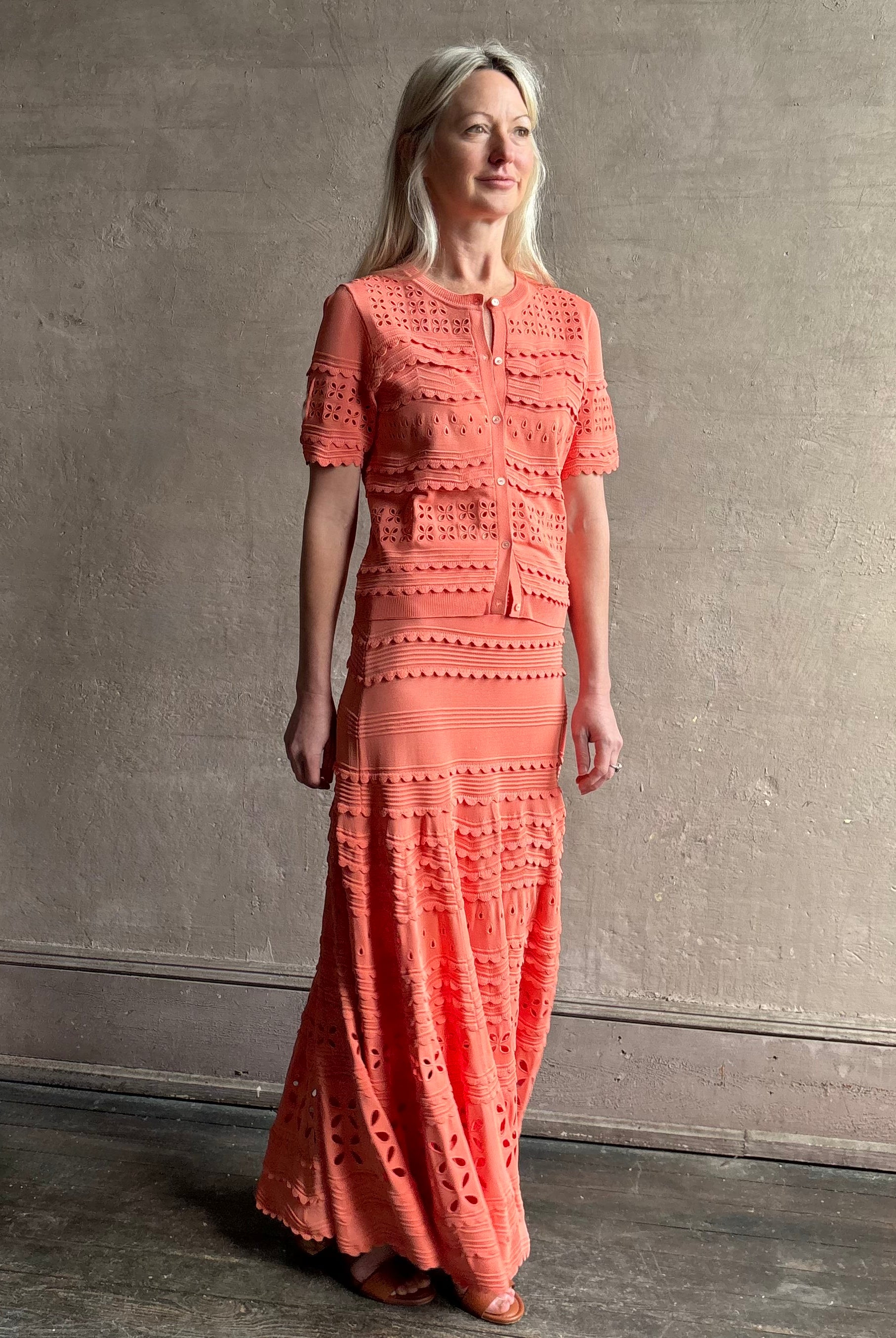 Woman wearing the feminine Annisa Eyelet Knit A-line maxi skirt from Ulla Johnson rendered in a luminous coral hue and crafted from luxury knit with matching top