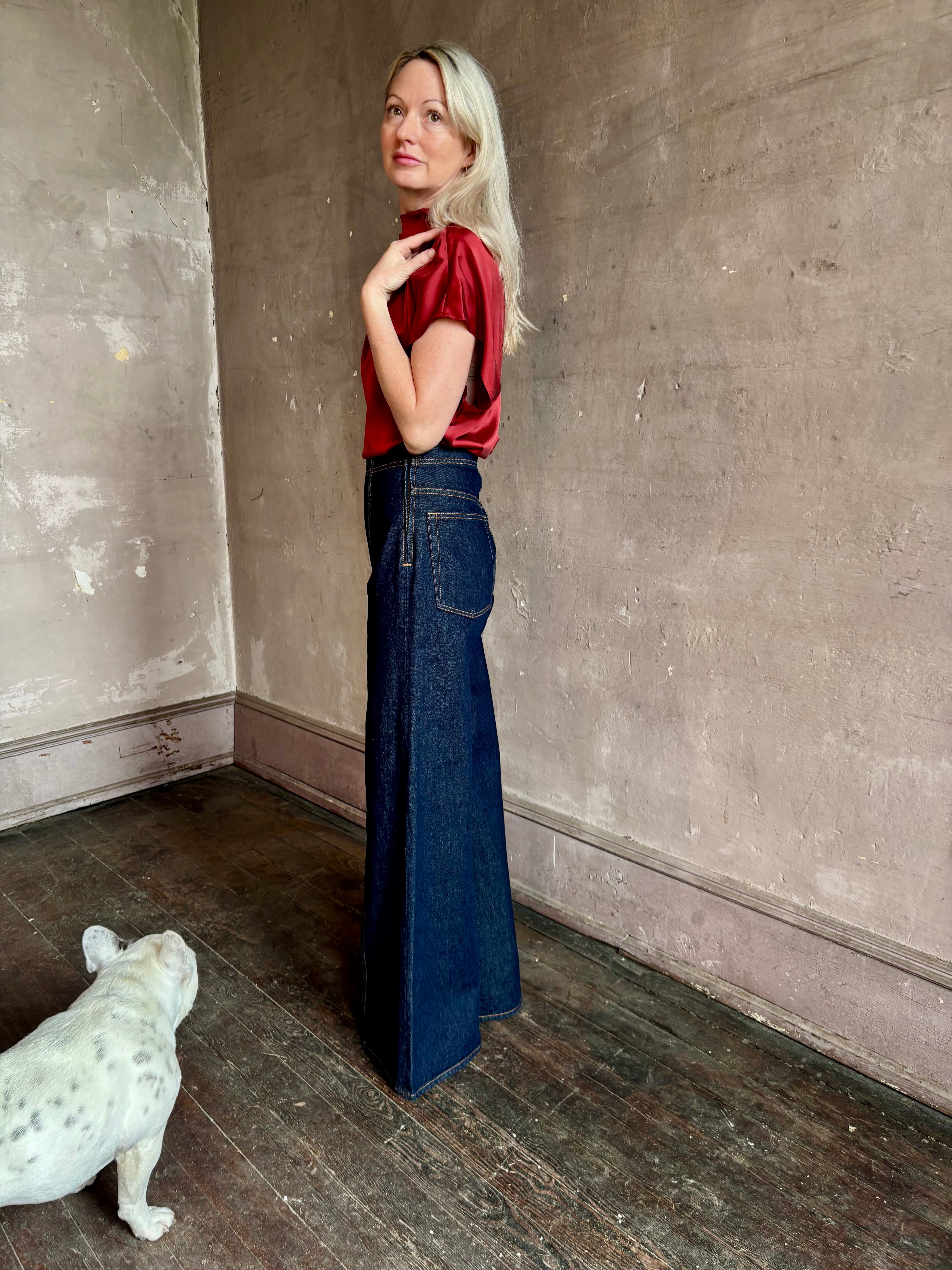 Mature woman wearing ULLA JOHNSON Bianca dark wash tigris rigid denim with a flat front, contrasting front seam details, high rise, wide leg, and side seam concealed zipper closure