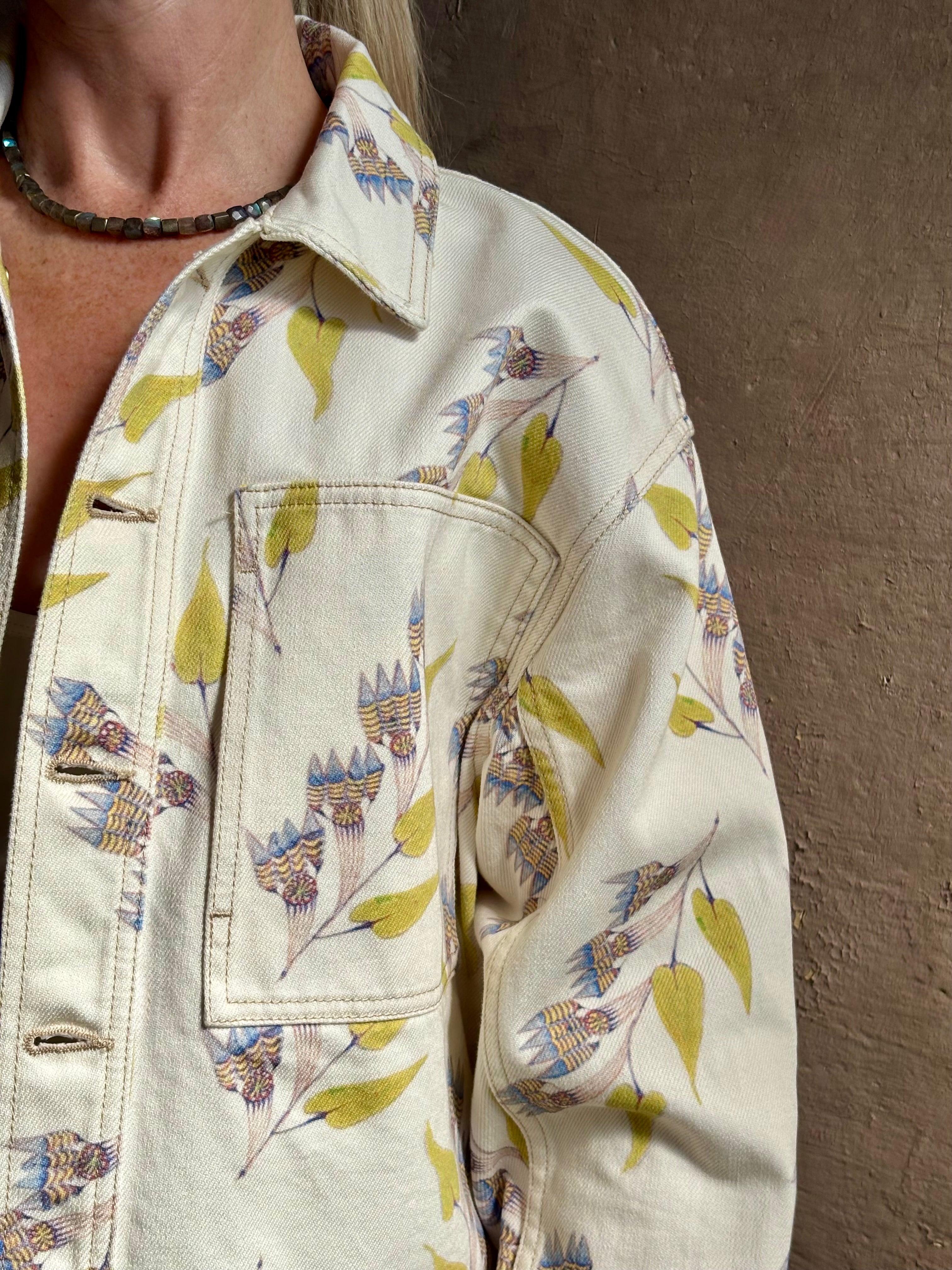 Mature woman wearing designer ULLA JOHNSON Bobbi cotton denim Jacket in an artisan collaboration print Infinite Flower with gold buttons, front pockets and crop length cool girl vibe