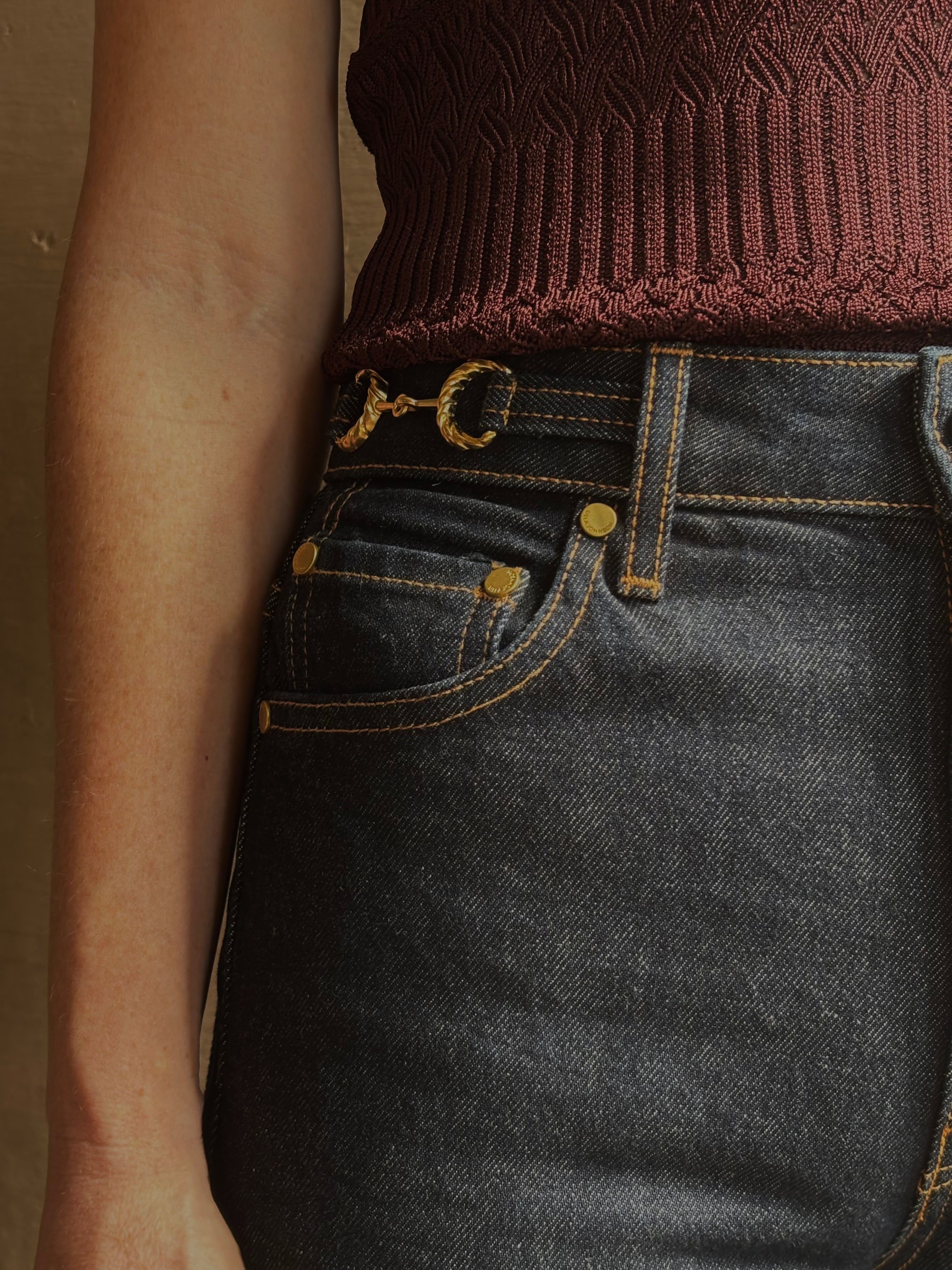 Mature woman wearing designer denim Colette Straight Leg Jean from Ulla Johnson offering American-made craftsmanship to a clean, timeless, and thoroughly modern everyday silhouette rendered in a sophisticated dark wash and crafted from 100% cotton with twisted buckle detail at waistband
