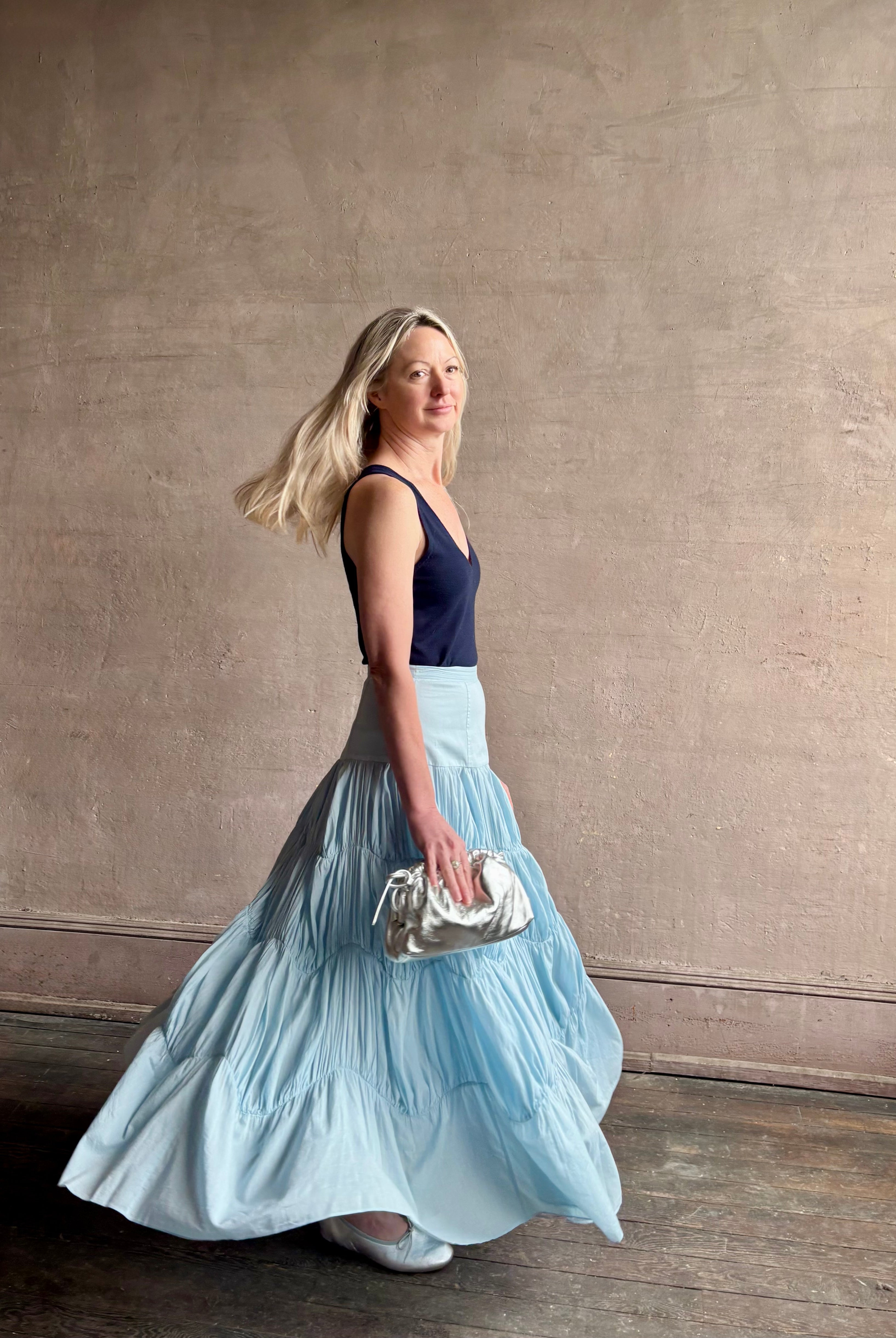 Mature woman wearing Davina Drop Waist Maxi Skirt from Ulla Johnson rendered in Adriatic Blue hue with intricate full skirt ruching