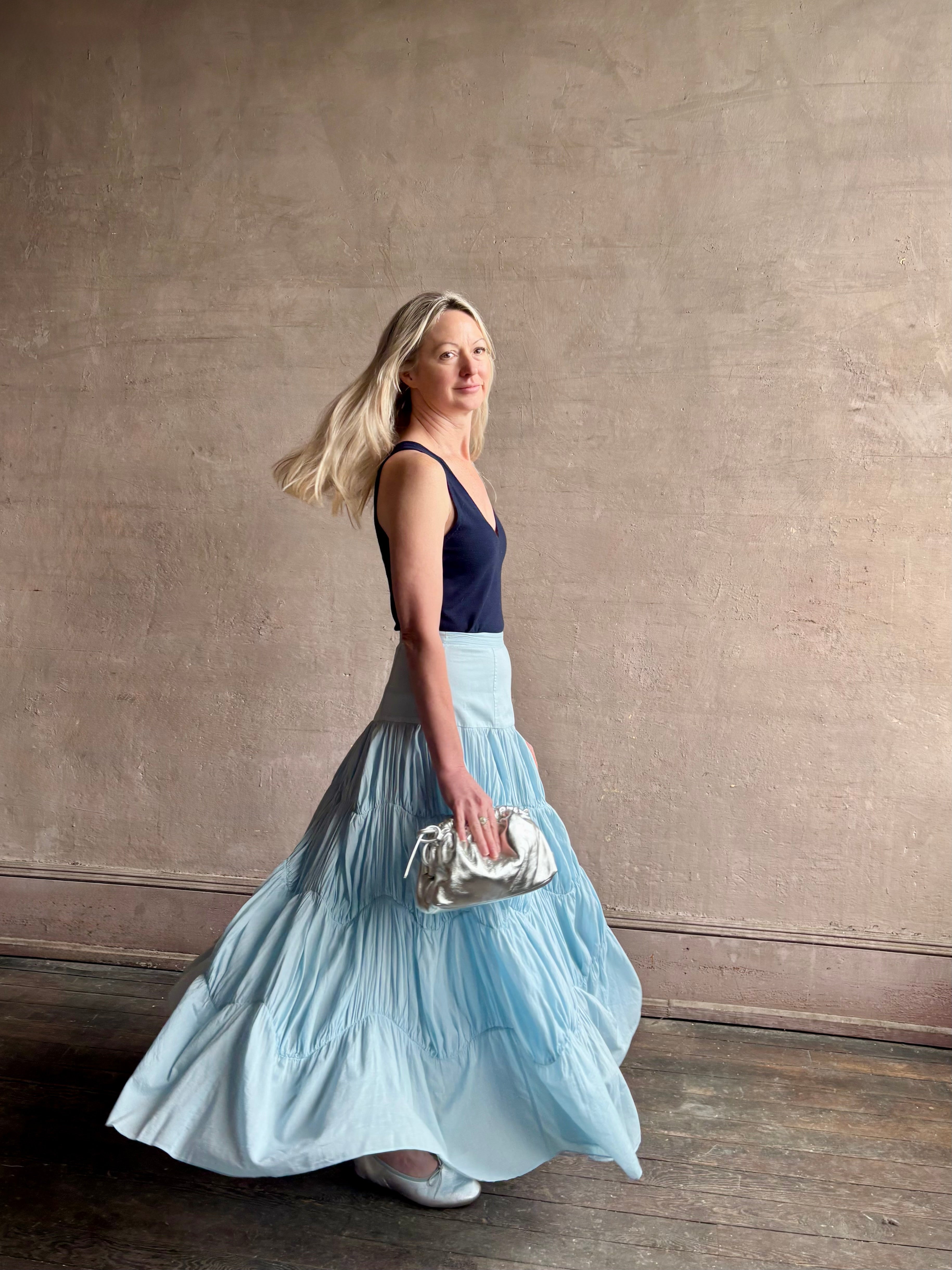 Mature woman wearing Davina Drop Waist Maxi Skirt from Ulla Johnson rendered in Adriatic Blue hue with intricate full skirt ruching