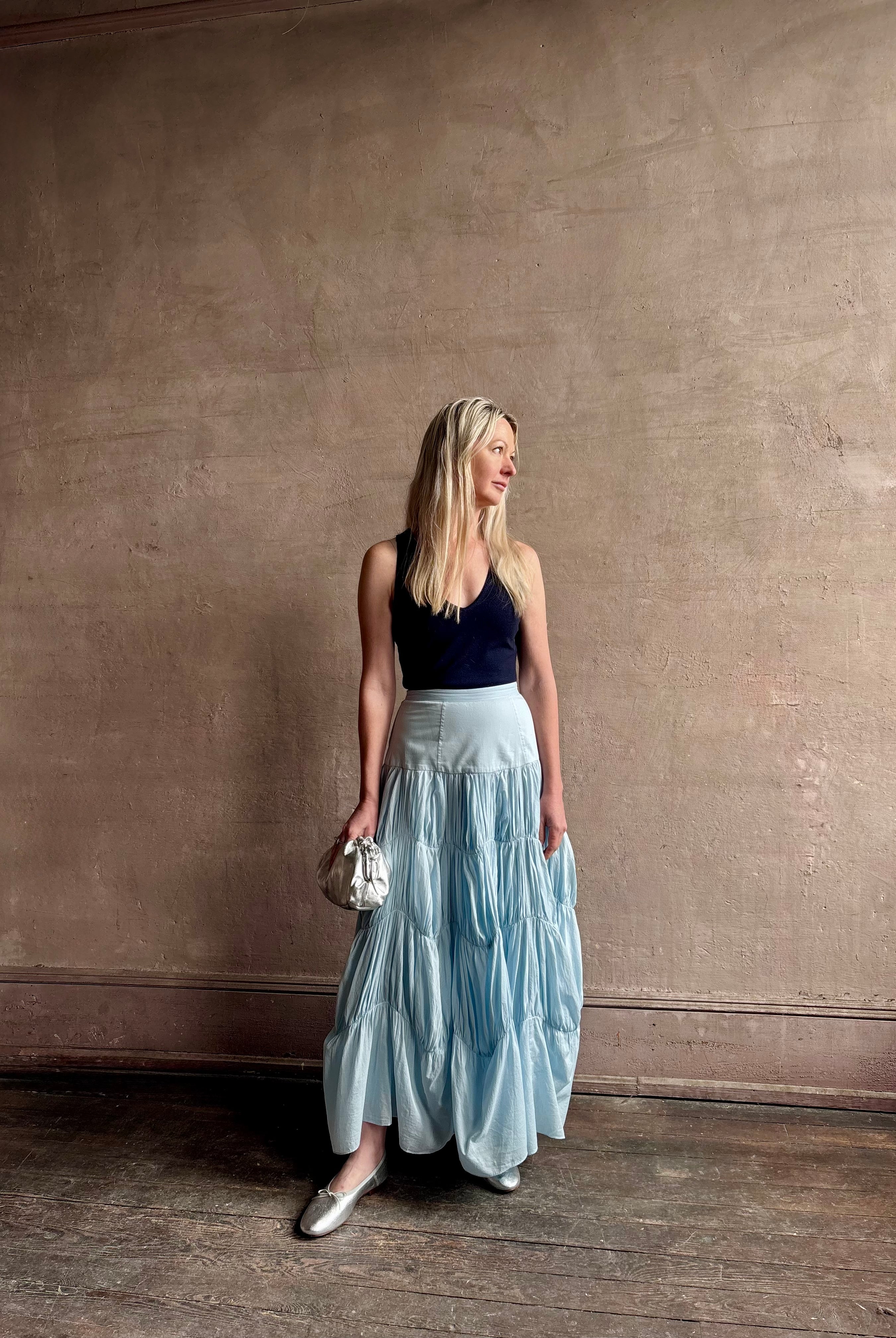 Mature woman wearing Davina Drop Waist Maxi Skirt from Ulla Johnson rendered in Adriatic Blue hue with intricate full skirt ruching