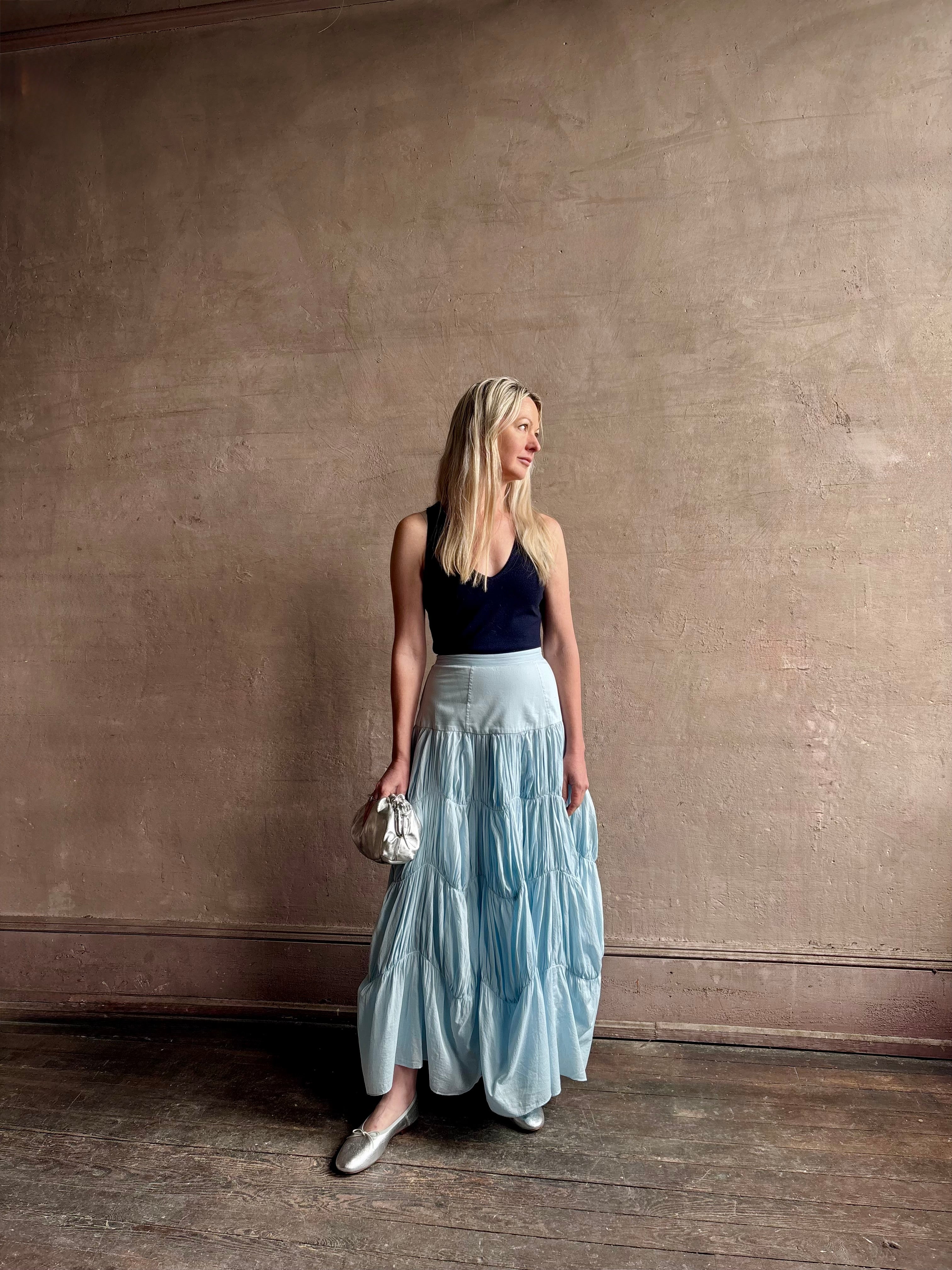 Mature woman wearing Davina Drop Waist Maxi Skirt from Ulla Johnson rendered in Adriatic Blue hue with intricate full skirt ruching