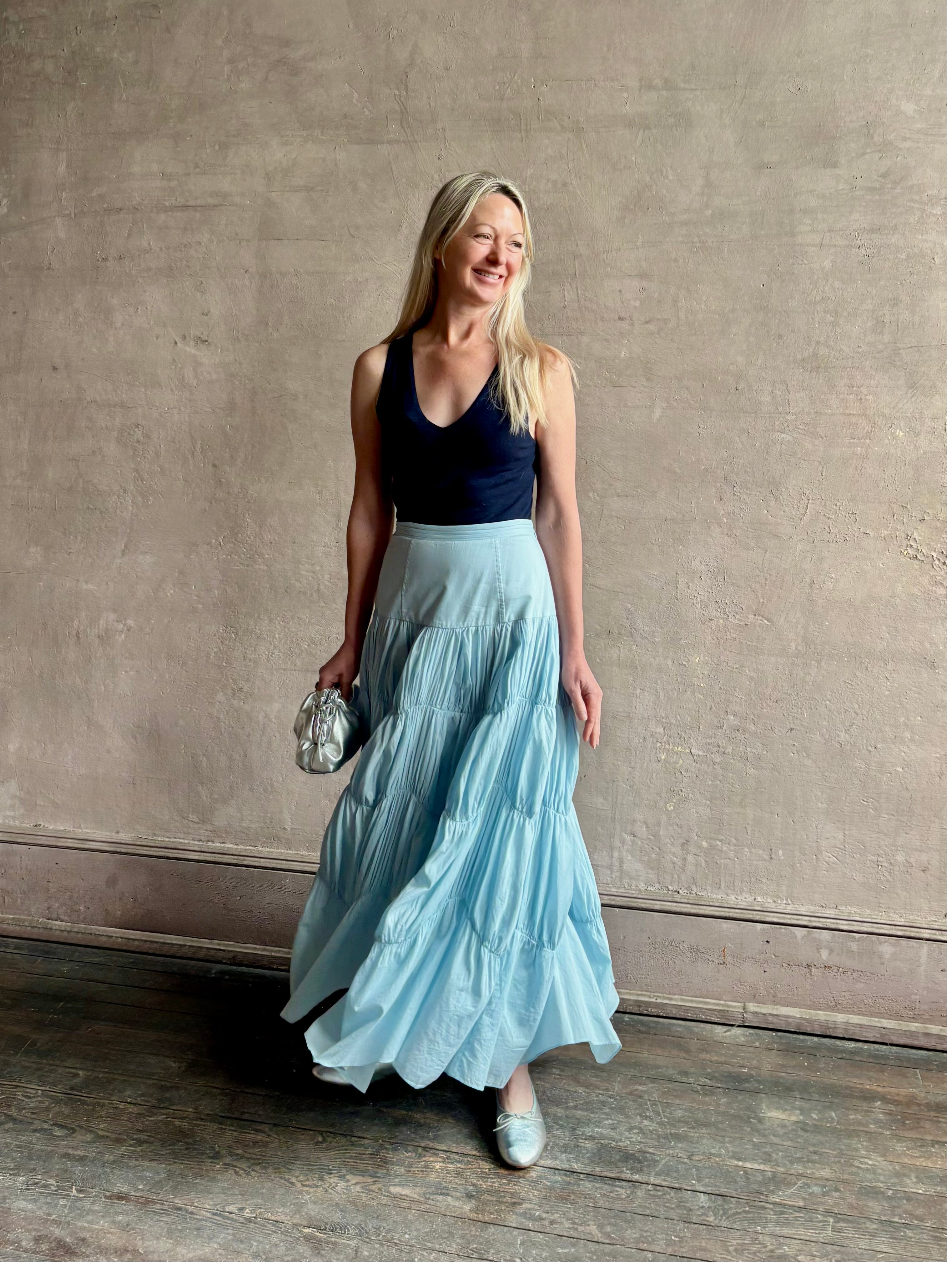 Mature woman wearing Davina Drop Waist Maxi Skirt from Ulla Johnson rendered in Adriatic Blue hue with intricate full skirt ruching
