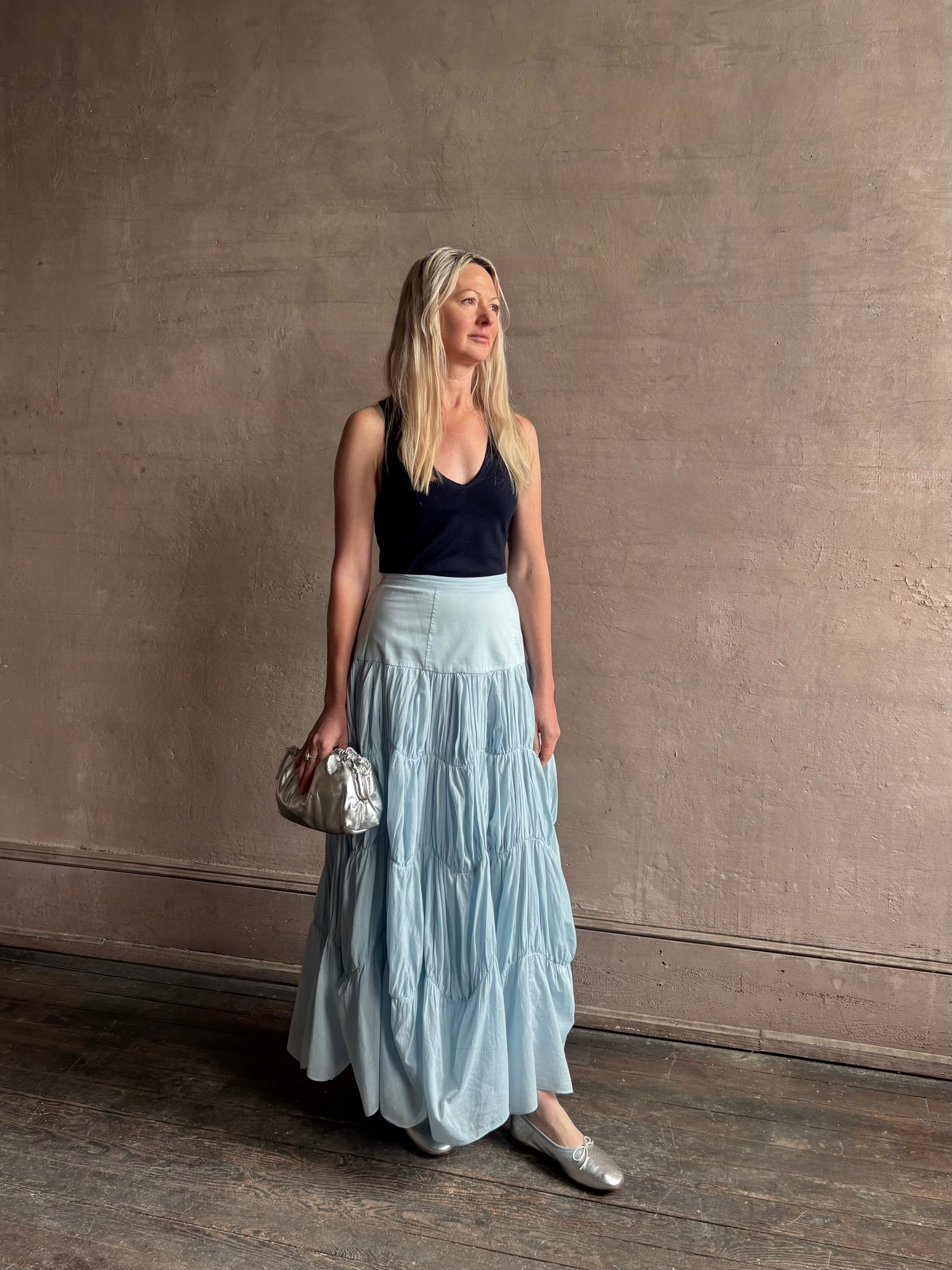 Mature woman wearing Davina Drop Waist Maxi Skirt from Ulla Johnson rendered in Adriatic Blue hue with intricate full skirt ruching