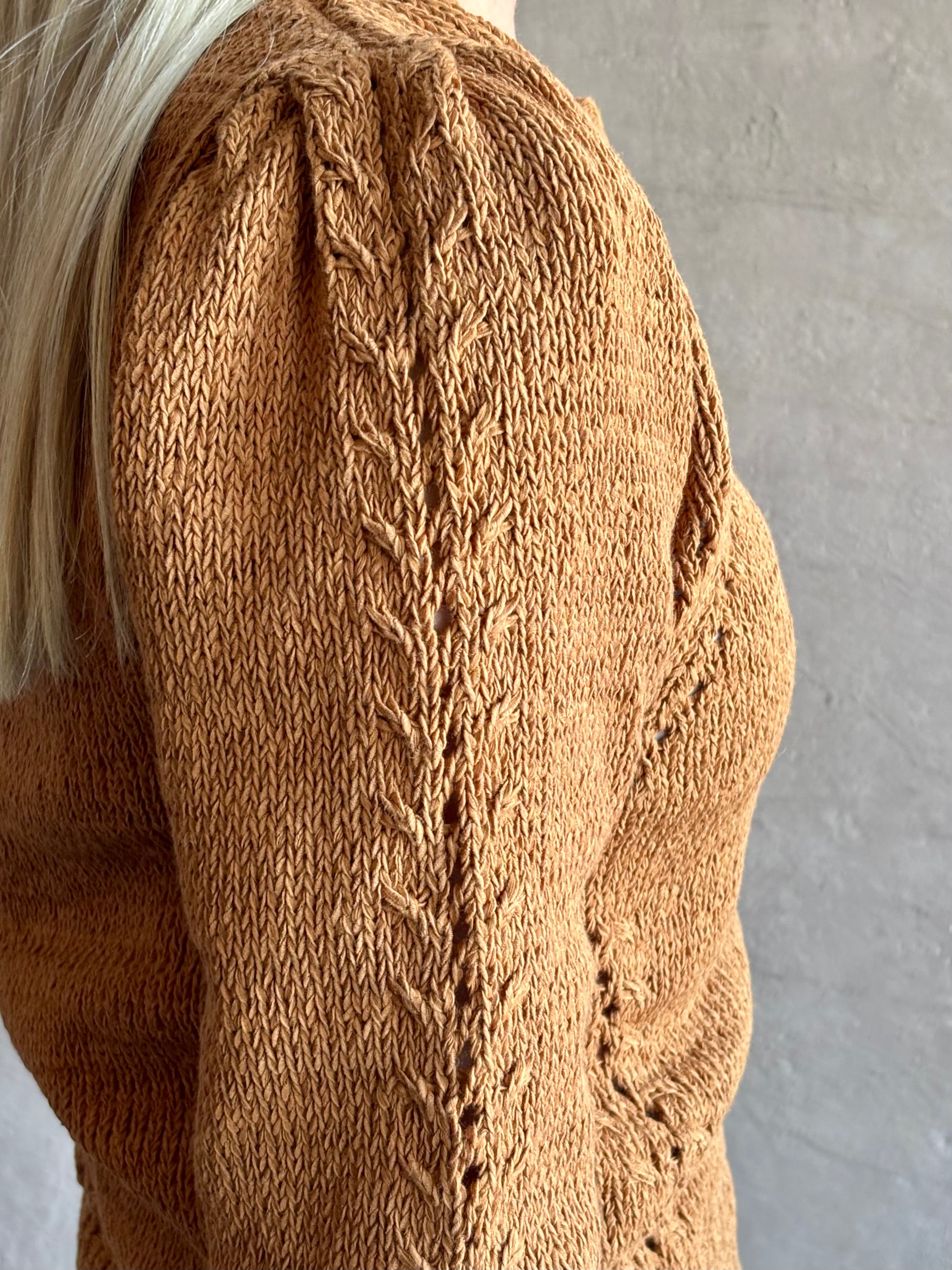 Mature woman wearing the Delphina Long Sleeve women's designer Cardigan from Ulla Johnson rendered in an umber hue with cable detail down sleeves