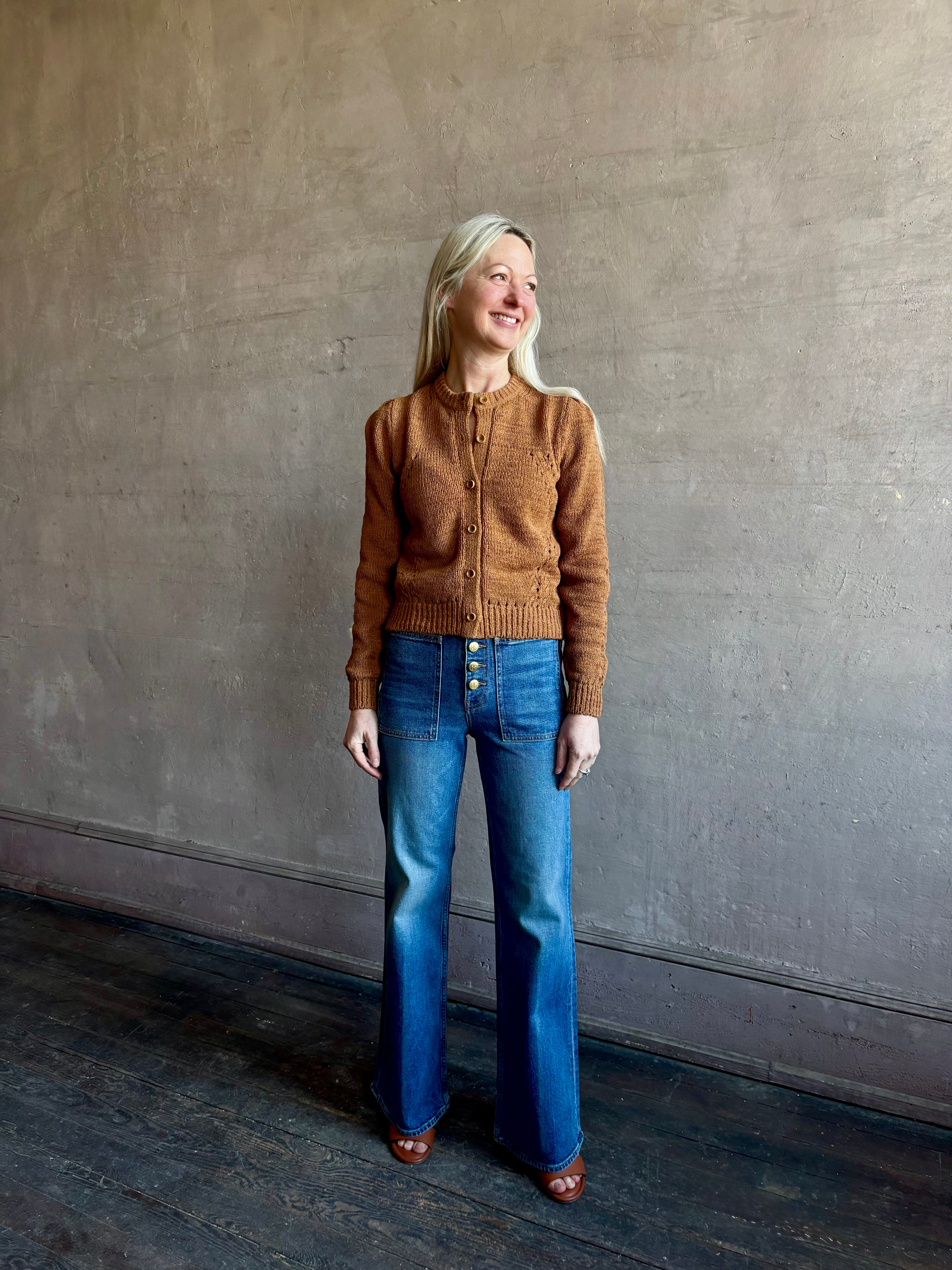 Mature woman wearing the Delphina Long Sleeve women's designer Cardigan from Ulla Johnson rendered in an umber hue with cable detail down sleeves