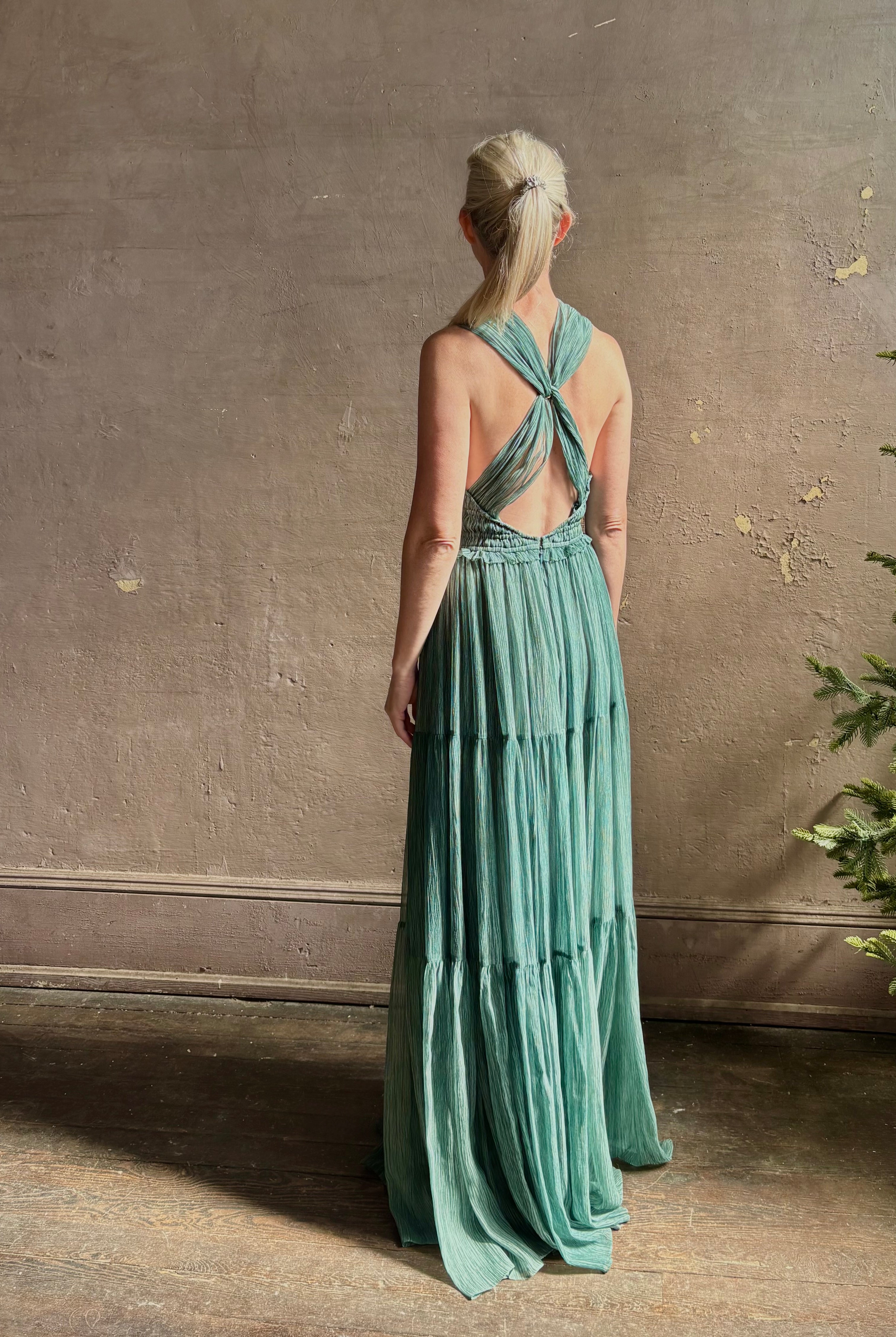 Woman wearing Freesia Gown from Ulla Johnson rendered in a soft green and crafted from luxurious silk crinkle chiffon with low back and flexible waistband