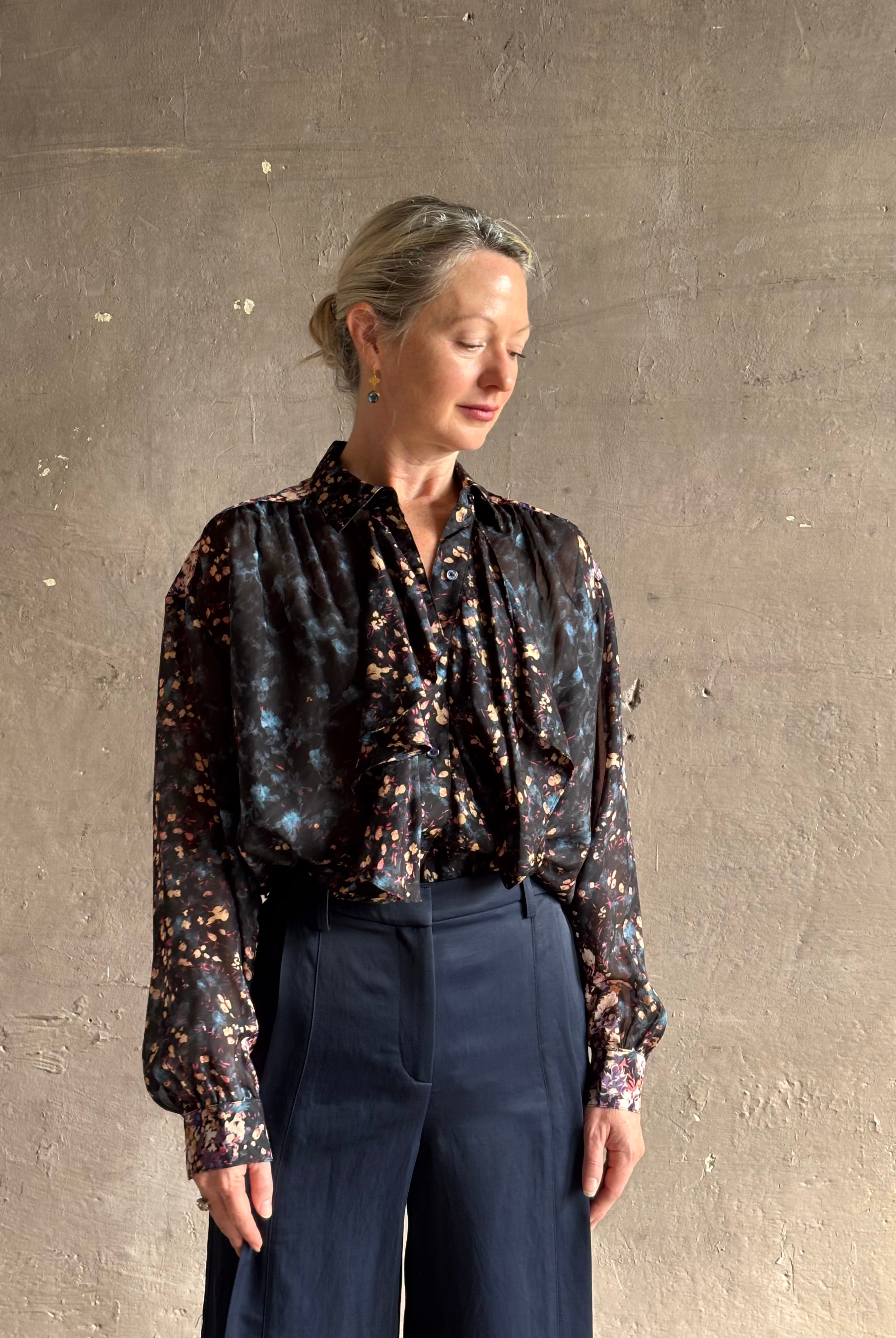 woman wearing designer Ulla Johnson long-sleeve black silk blouse subtle floral print collared button front ruffle detail