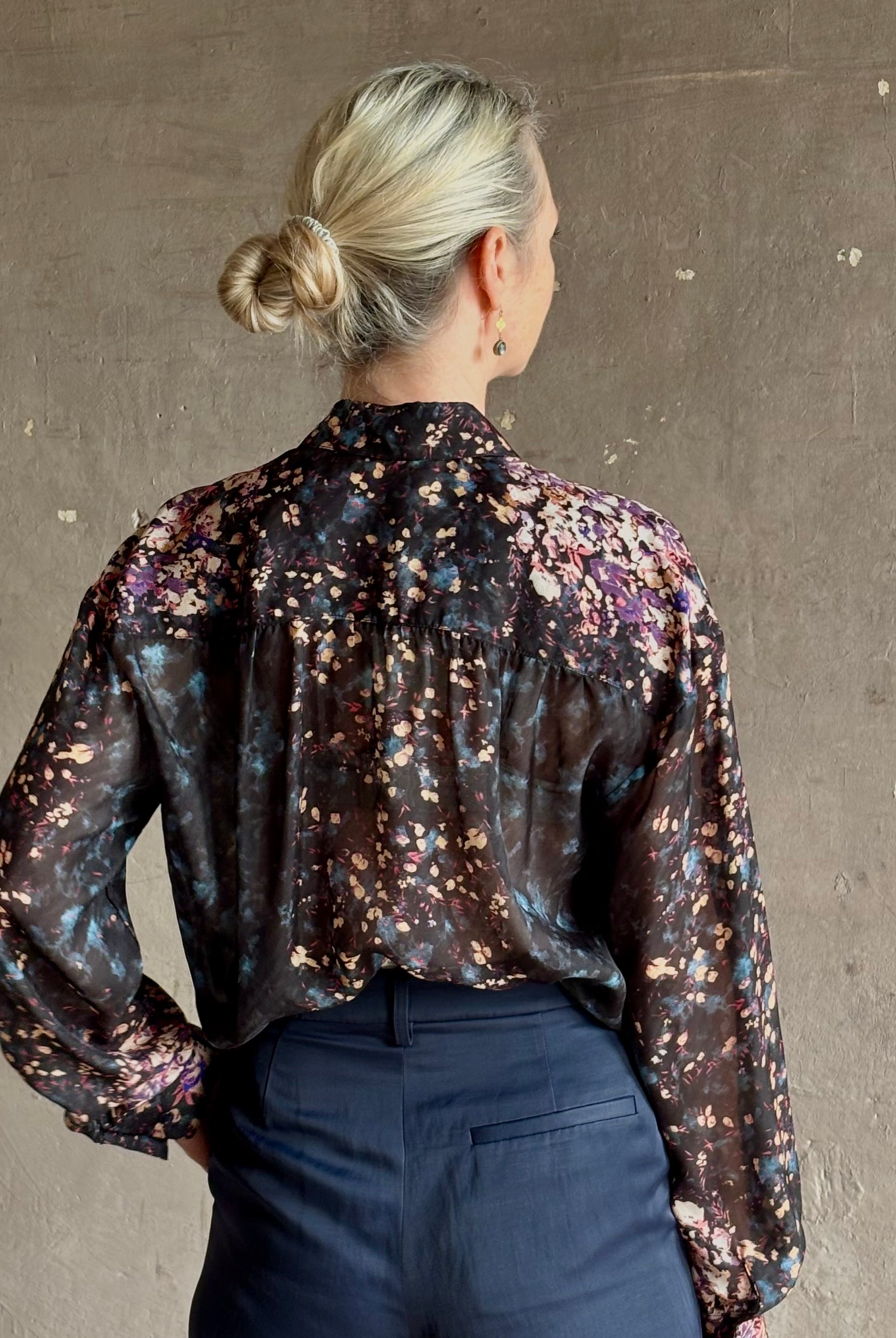 woman wearing Ulla Johnson long-sleeve black silk blouse subtle floral print collared button front ruffle detail