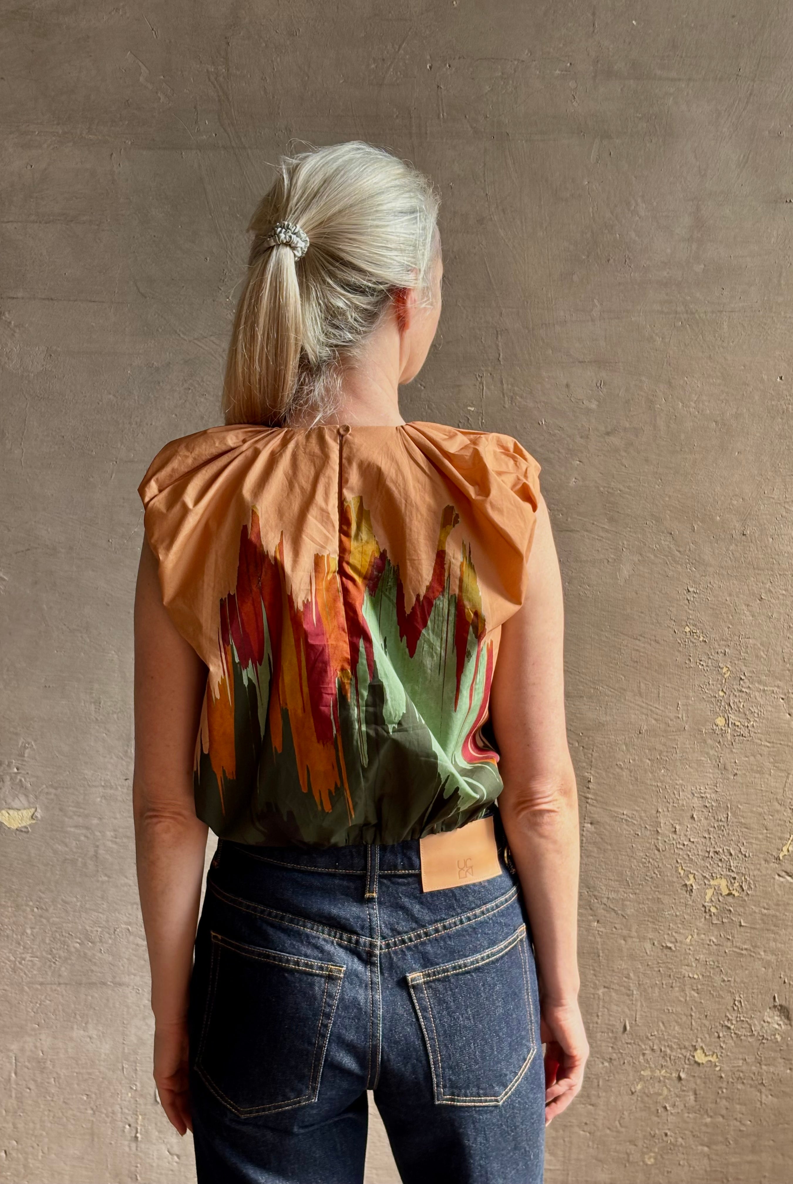 Mature woman wearing Women's designer Gracie sleeveless Cotton Top from Ulla Johnson rendered in a rich abstract Agate print composed of dark green, mint green, burgundy, terra cotta, and sienna and crafted from lightweight cotton poplin