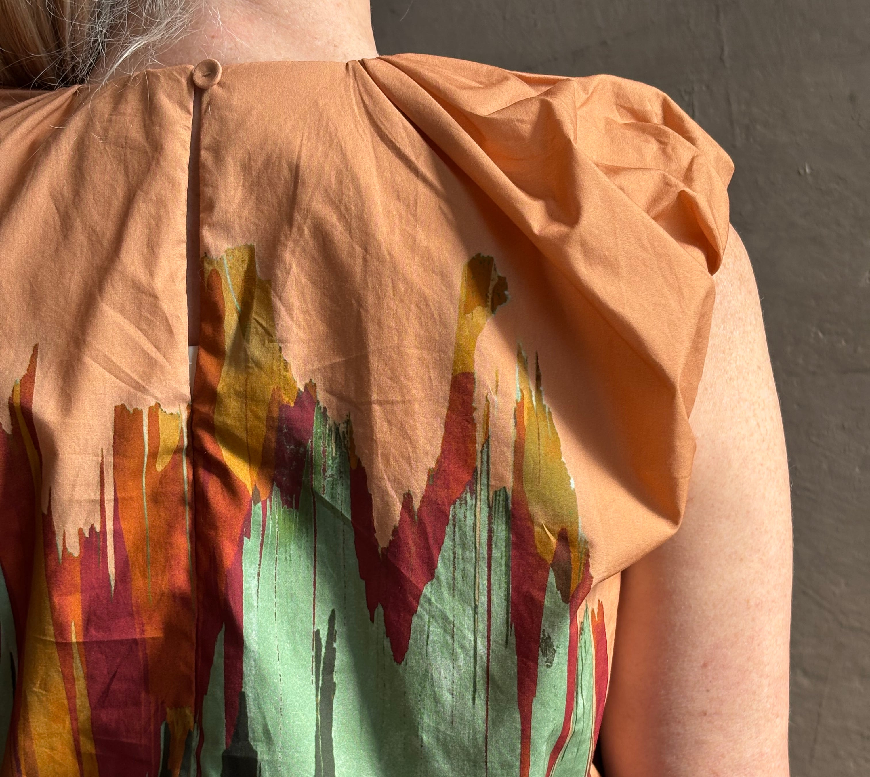 Mature woman wearing Women's designer Gracie sleeveless Cotton Top from Ulla Johnson rendered in a rich abstract Agate print composed of dark green, mint green, burgundy, terra cotta, and sienna and crafted from lightweight cotton poplin