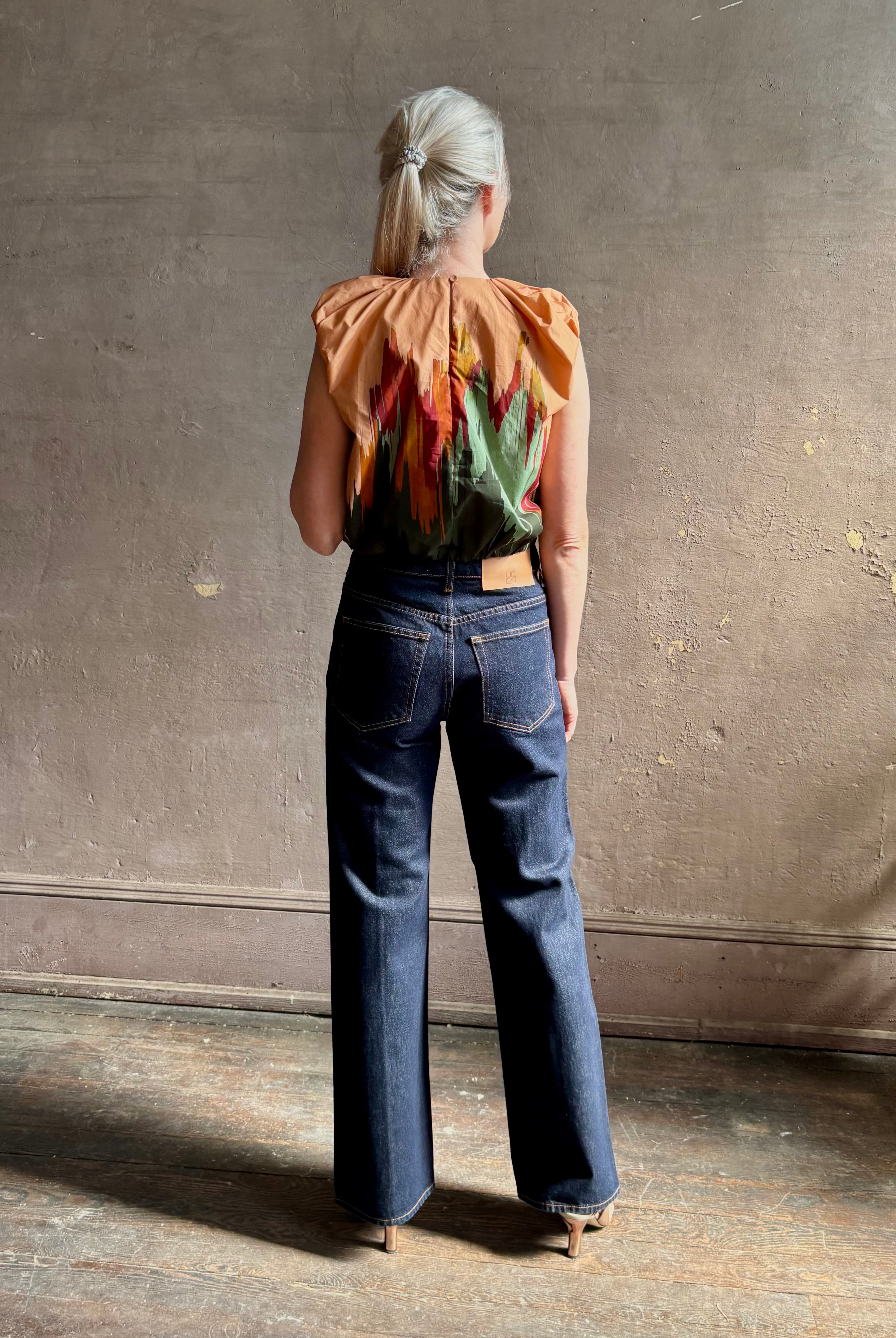 Mature woman wearing Women's designer Gracie sleeveless Cotton Top from Ulla Johnson rendered in a rich abstract Agate print composed of dark green, mint green, burgundy, terra cotta, and sienna and crafted from lightweight cotton poplin