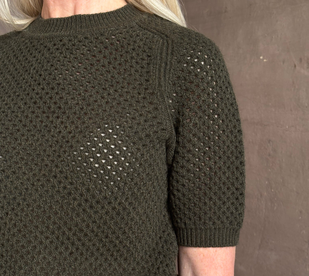 Mature woman wearing designer Ulla Johnson Imara Short Sleeve dark green Sweater with a dimensional open weave