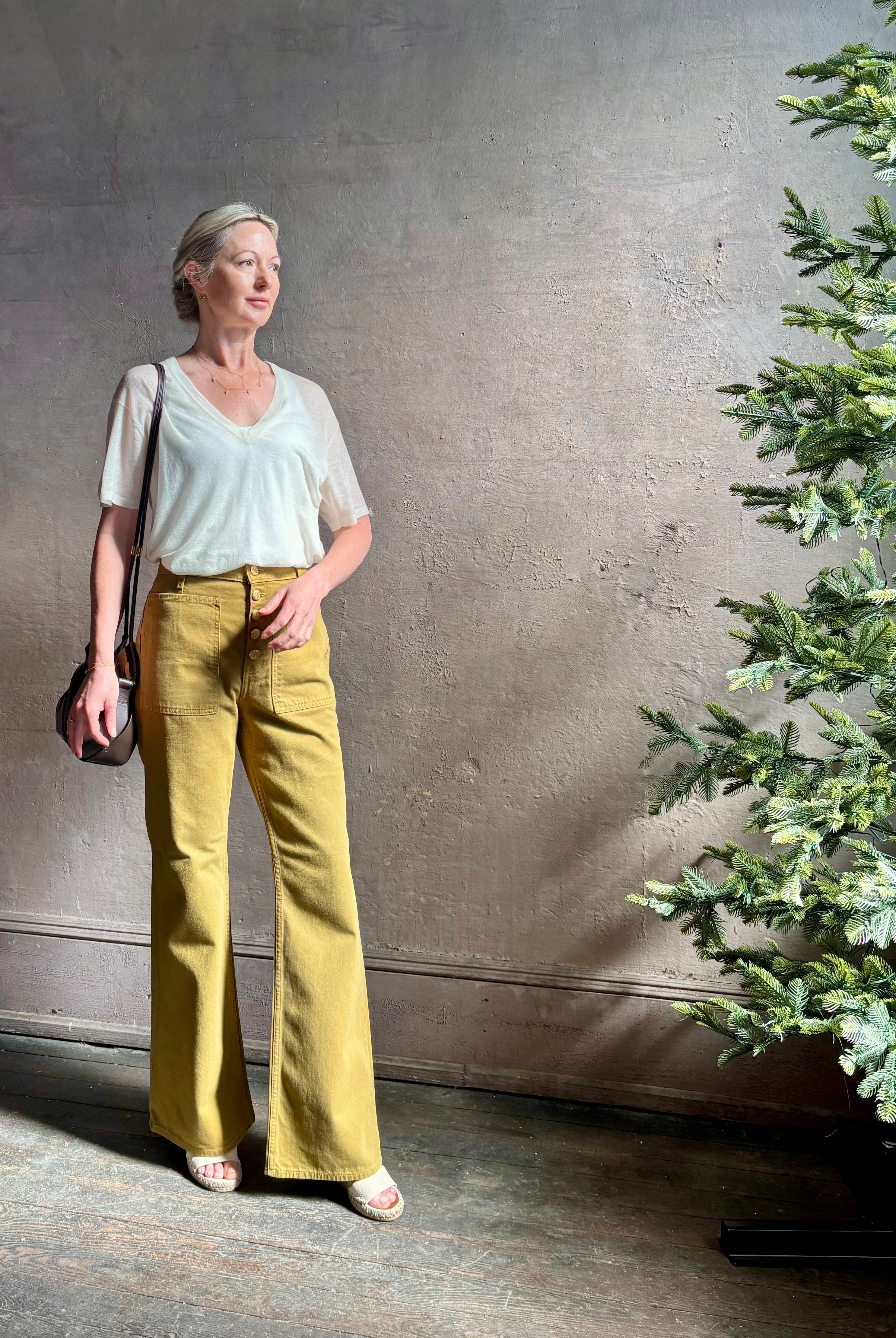 Mature woman wearing luxury Ulla Johnson Lou cotton rigid full length green denim with gold button fly patch pocket