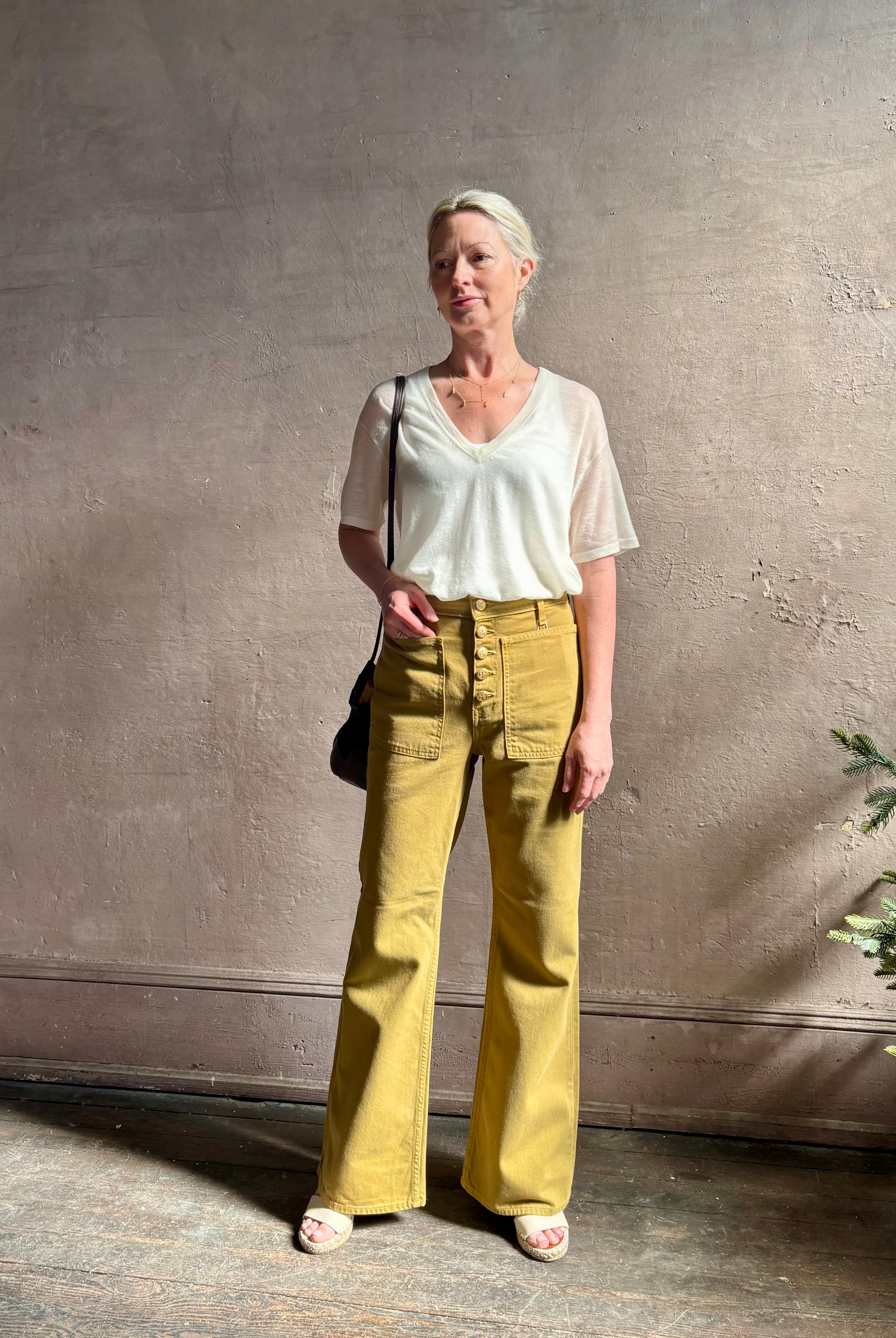 Mature woman wearing luxury Ulla Johnson Lou cotton rigid full length green denim with gold button fly patch pocket