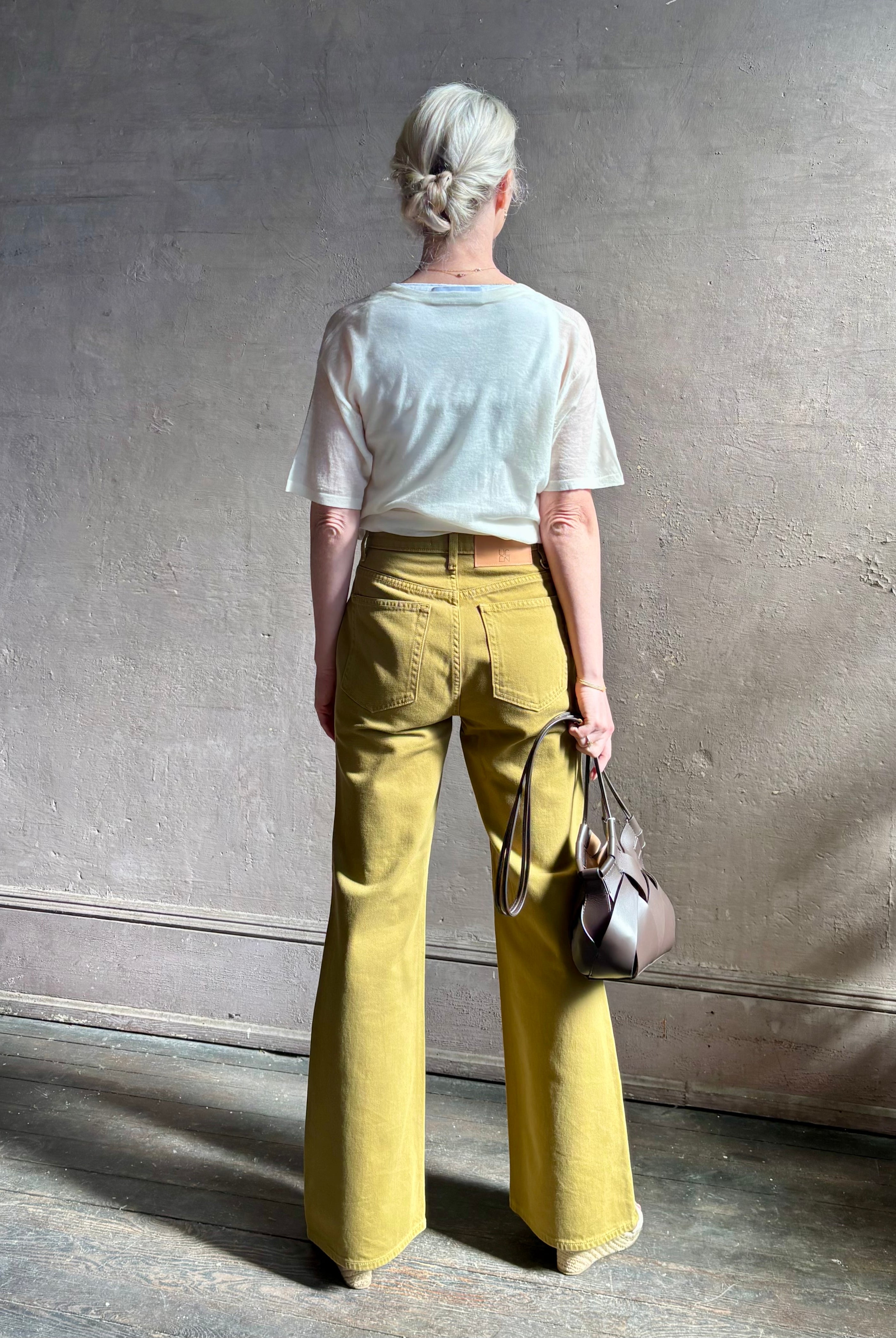 Mature woman wearing luxury Ulla Johnson Lou cotton rigid full length green denim with gold button fly patch pocket