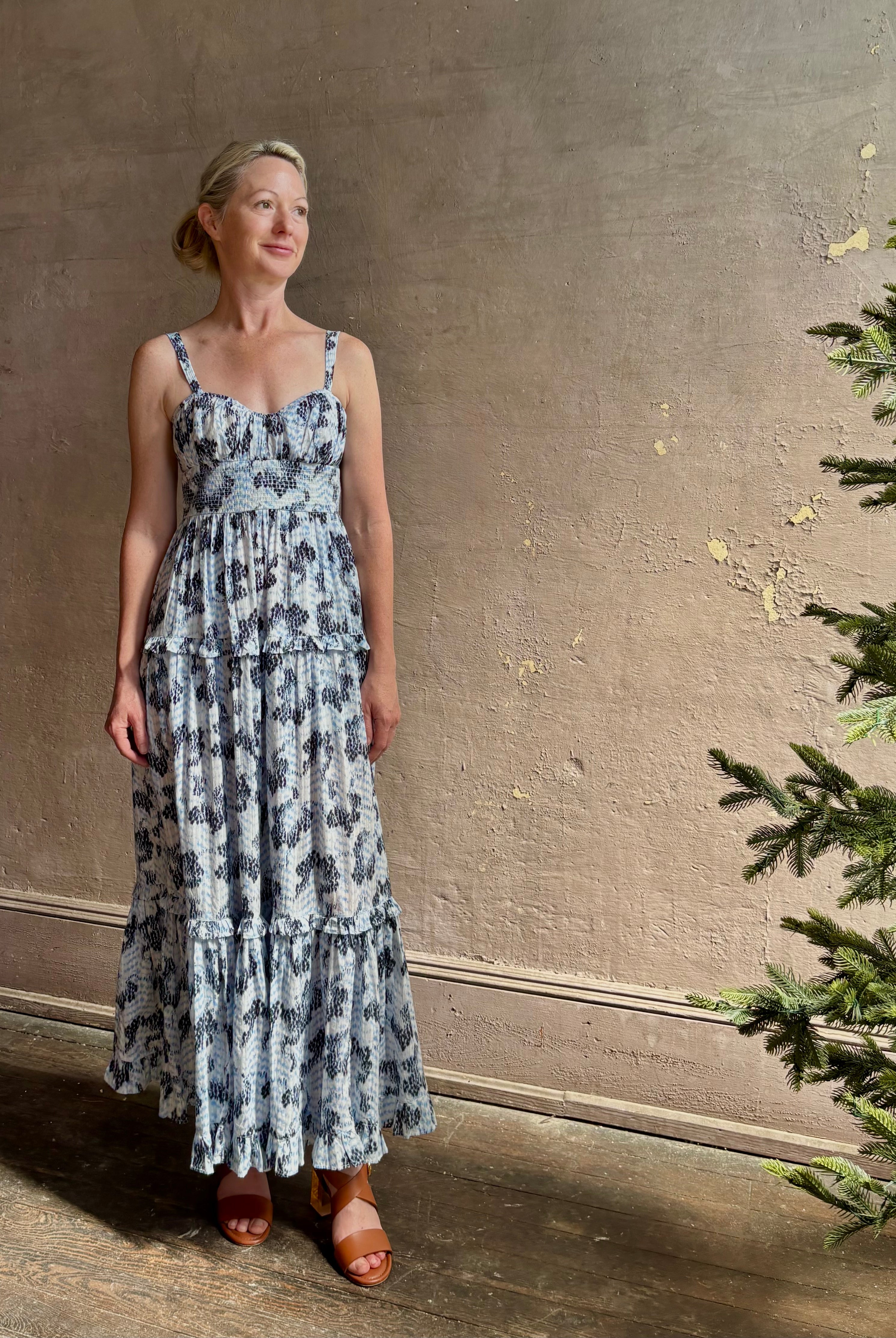 Mature woman wearing Ophelia Cami Cotton maxi Dress from Ulla Johnson rendered in a crisp white ground adorned with a soft black and light blue print and crafted from a cotton and viscose blend with an empire waist, sweatheart neckline and spaghetti straps