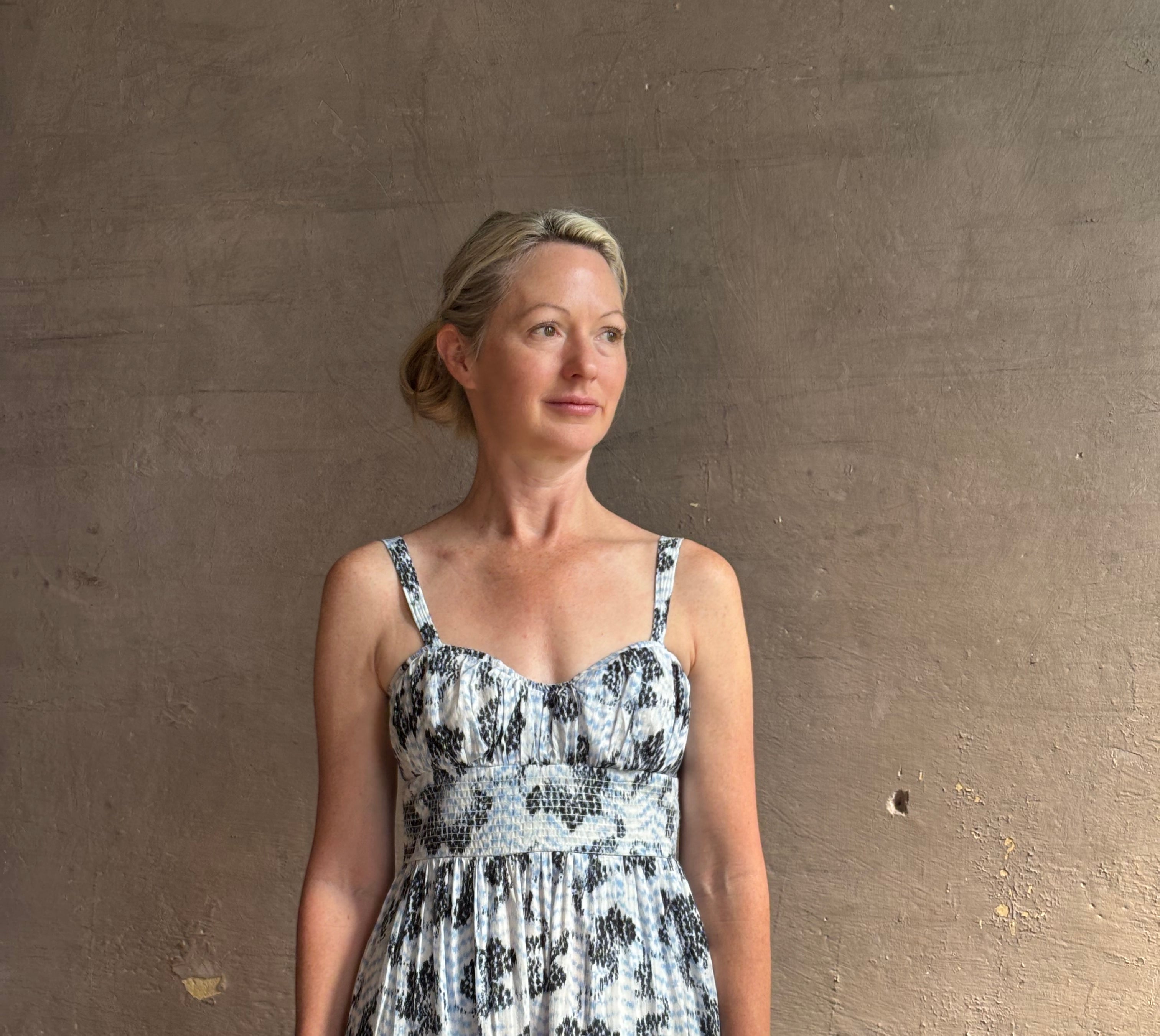 Mature woman wearing Ophelia Cami Cotton maxi Dress from Ulla Johnson rendered in a crisp white ground adorned with a soft black and light blue print and crafted from a cotton and viscose blend with an empire waist, sweatheart neckline and spaghetti straps