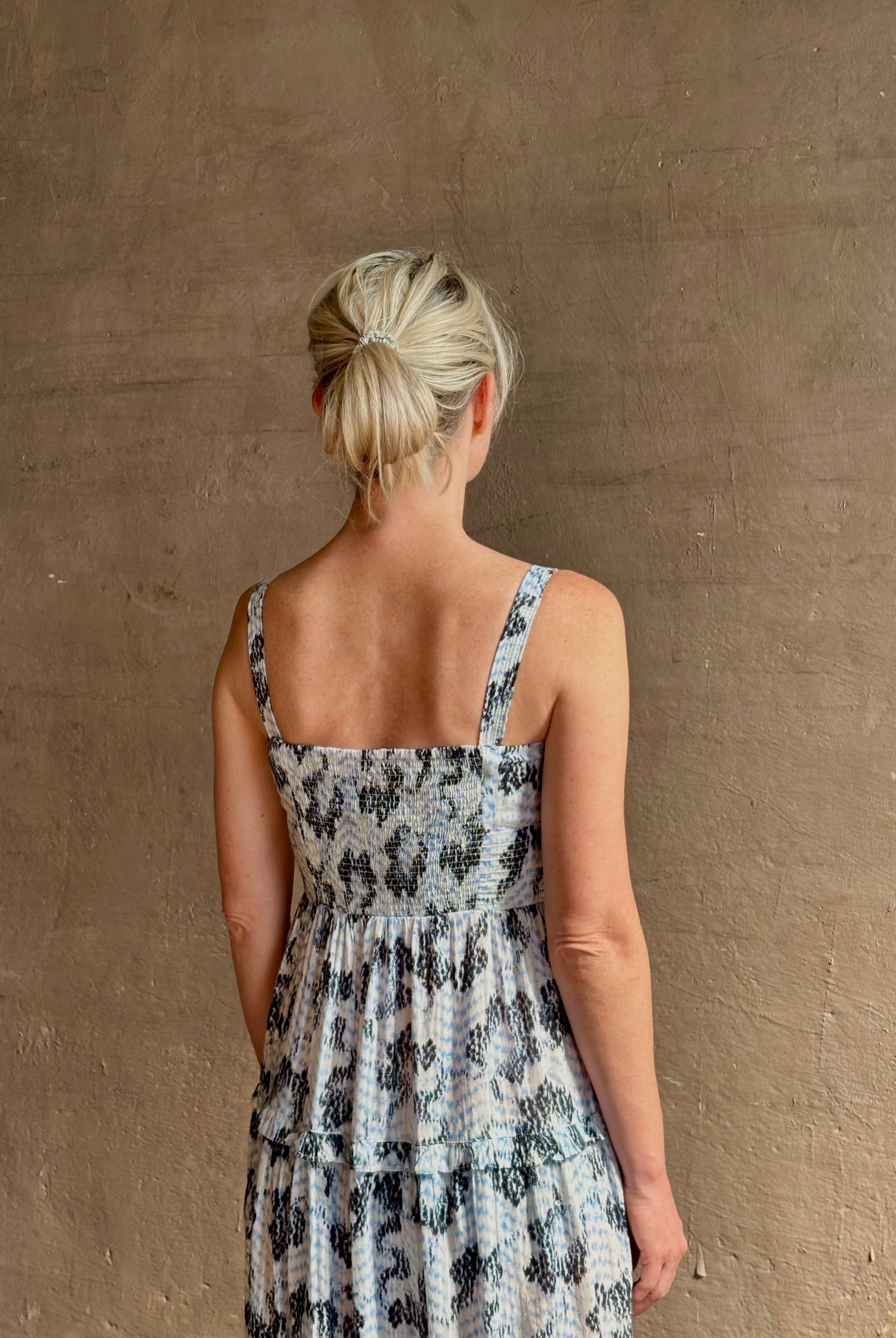 Mature woman wearing Ophelia Cami Cotton maxi Dress from Ulla Johnson rendered in a crisp white ground adorned with a soft black and light blue print and crafted from a cotton and viscose blend with an empire waist, sweatheart neckline and spaghetti straps