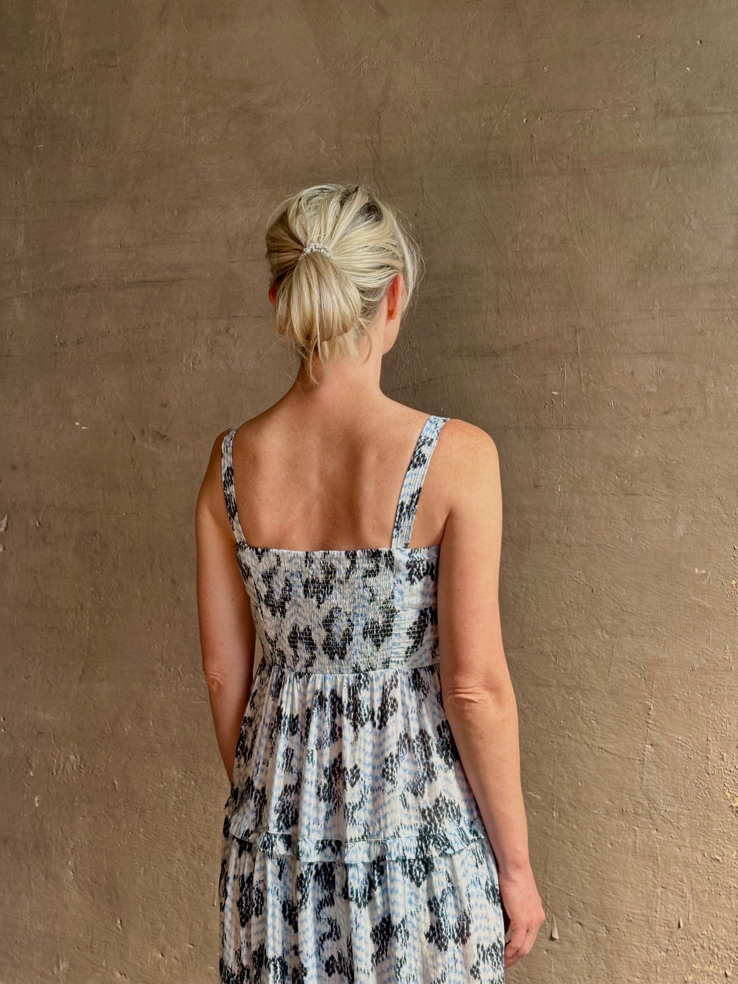 Mature woman wearing Ophelia Cami Cotton maxi Dress from Ulla Johnson rendered in a crisp white ground adorned with a soft black and light blue print and crafted from a cotton and viscose blend with an empire waist, sweatheart neckline and spaghetti straps