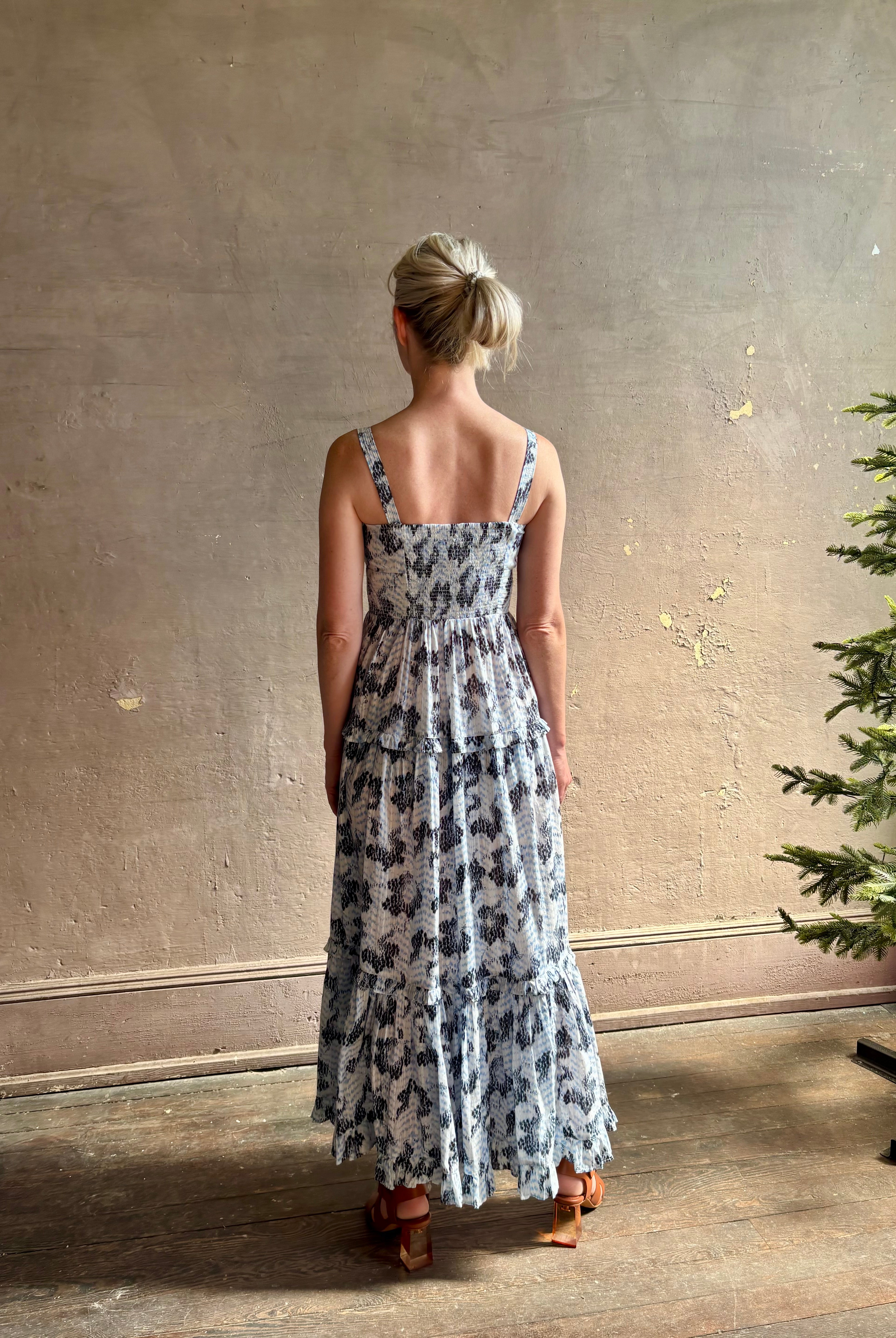 Mature woman wearing Ophelia Cami Cotton maxi Dress from Ulla Johnson rendered in a crisp white ground adorned with a soft black and light blue print and crafted from a cotton and viscose blend with an empire waist, sweatheart neckline and spaghetti straps