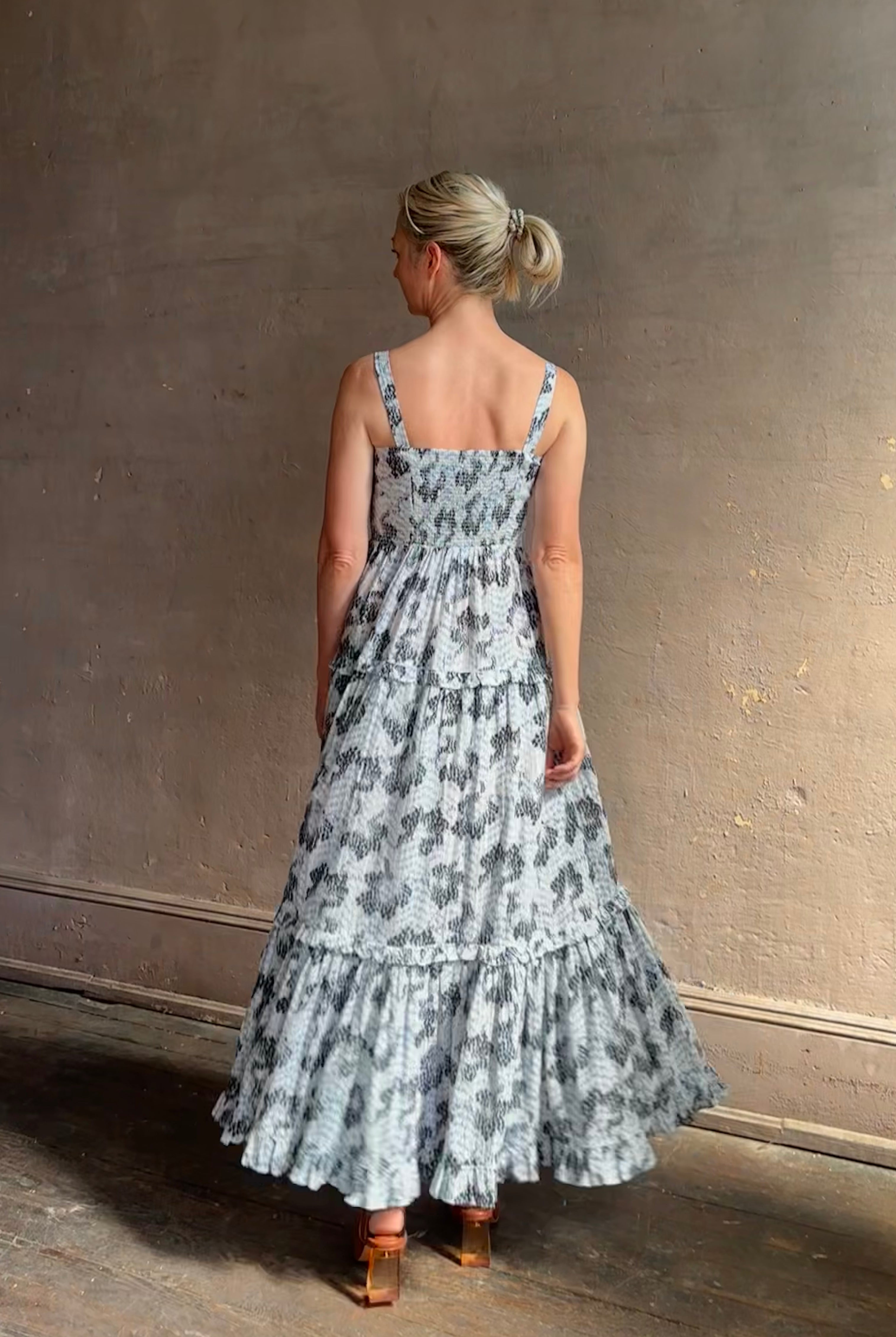 Mature woman wearing Ophelia Cami Cotton maxi Dress from Ulla Johnson rendered in a crisp white ground adorned with a soft black and light blue print and crafted from a cotton and viscose blend with an empire waist, sweatheart neckline and spaghetti straps