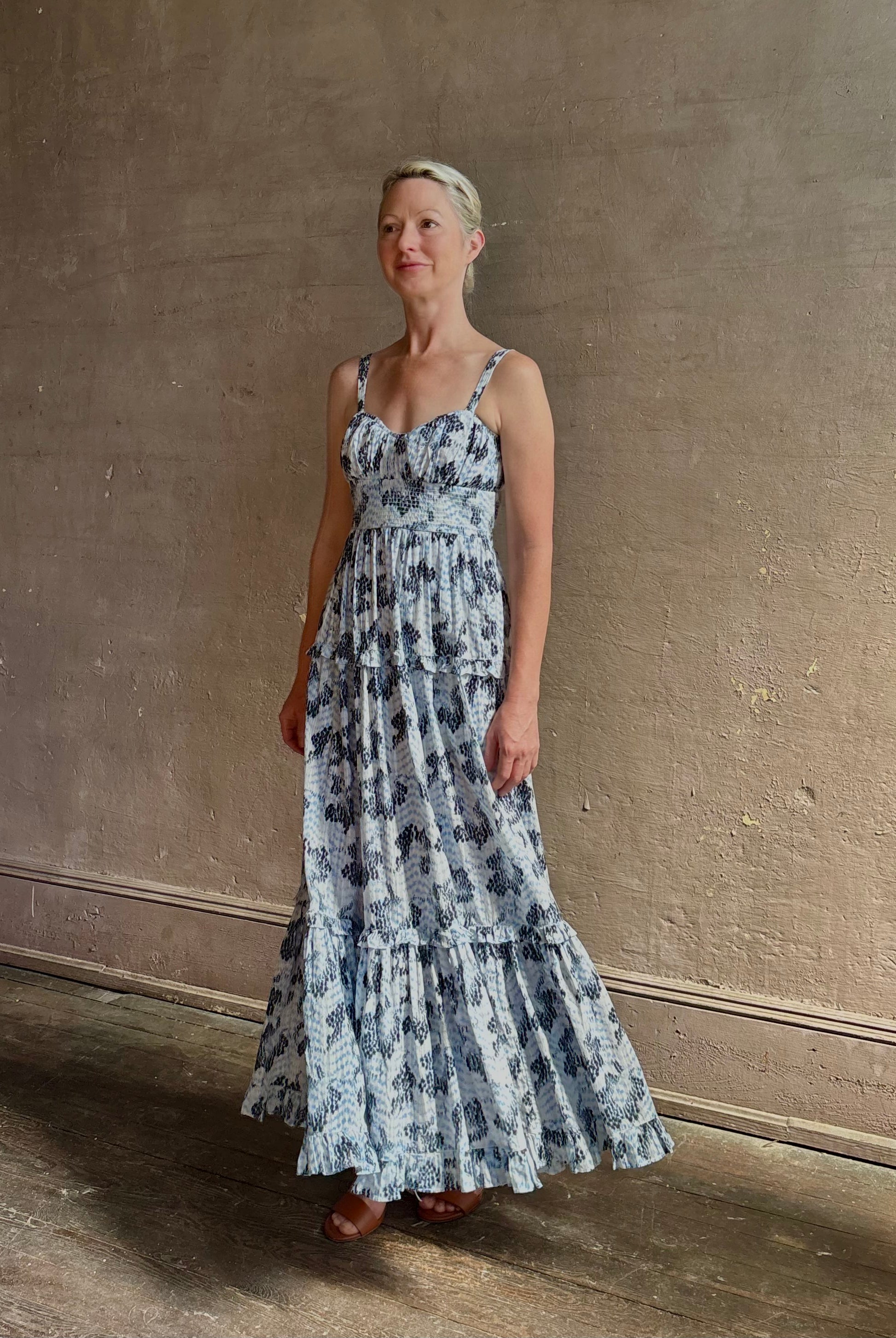 Mature woman wearing Ophelia Cami Cotton maxi Dress from Ulla Johnson rendered in a crisp white ground adorned with a soft black and light blue print and crafted from a cotton and viscose blend with an empire waist, sweatheart neckline and spaghetti straps