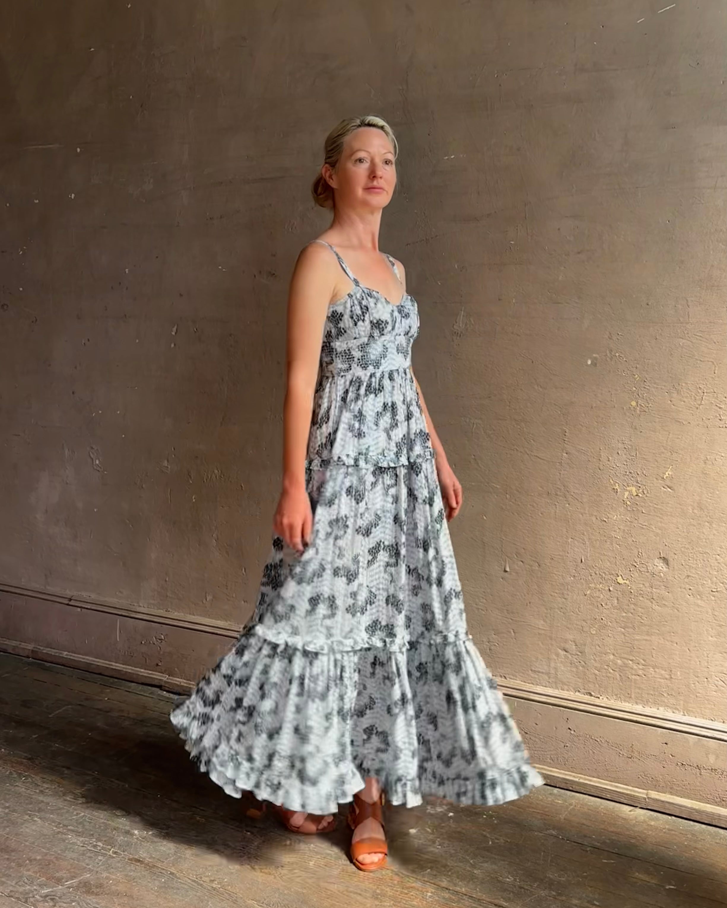 Mature woman wearing Ophelia Cami Cotton maxi Dress from Ulla Johnson rendered in a crisp white ground adorned with a soft black and light blue print and crafted from a cotton and viscose blend with an empire waist, sweatheart neckline and spaghetti straps