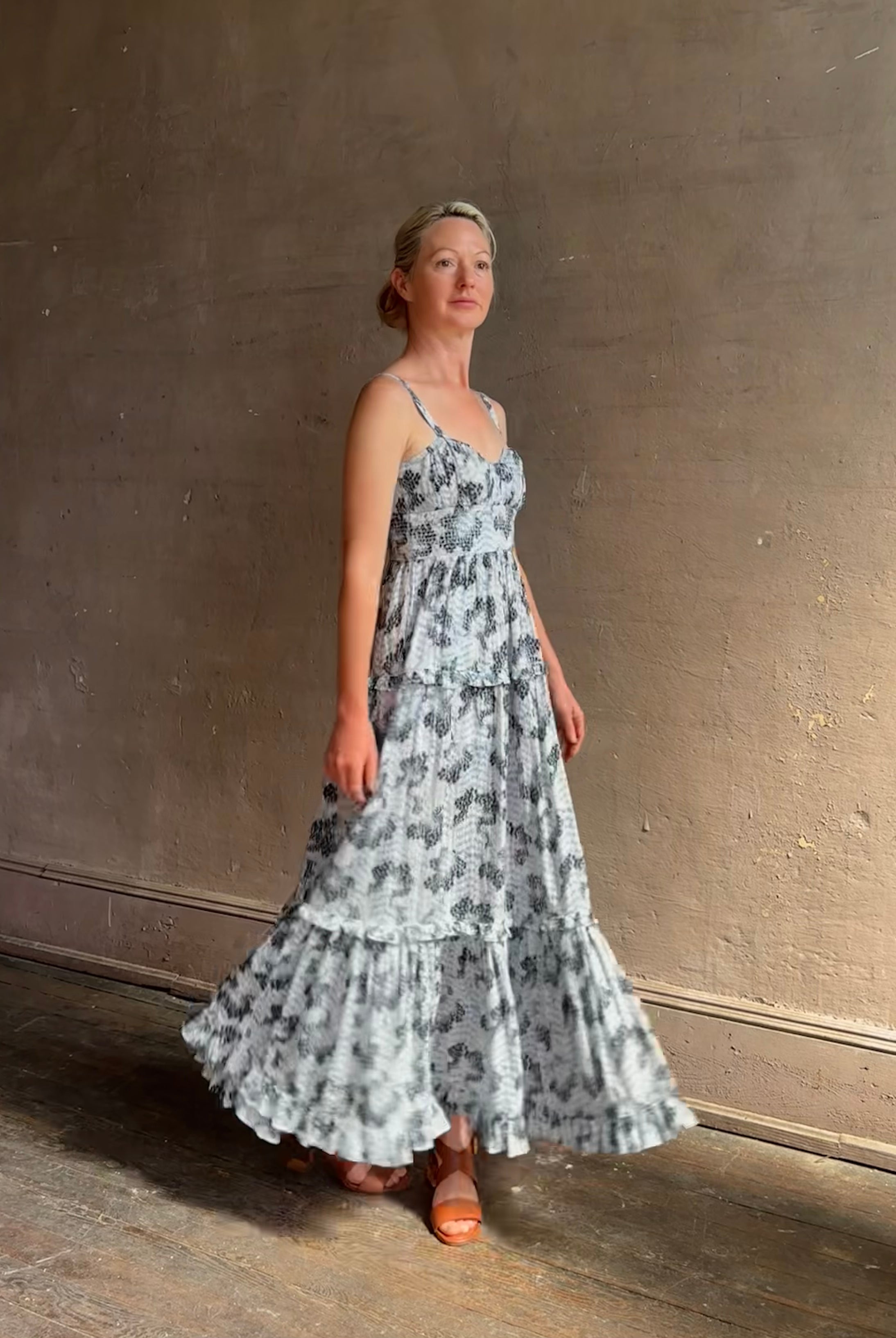 Mature woman wearing Ophelia Cami Cotton maxi Dress from Ulla Johnson rendered in a crisp white ground adorned with a soft black and light blue print and crafted from a cotton and viscose blend with an empire waist, sweatheart neckline and spaghetti straps