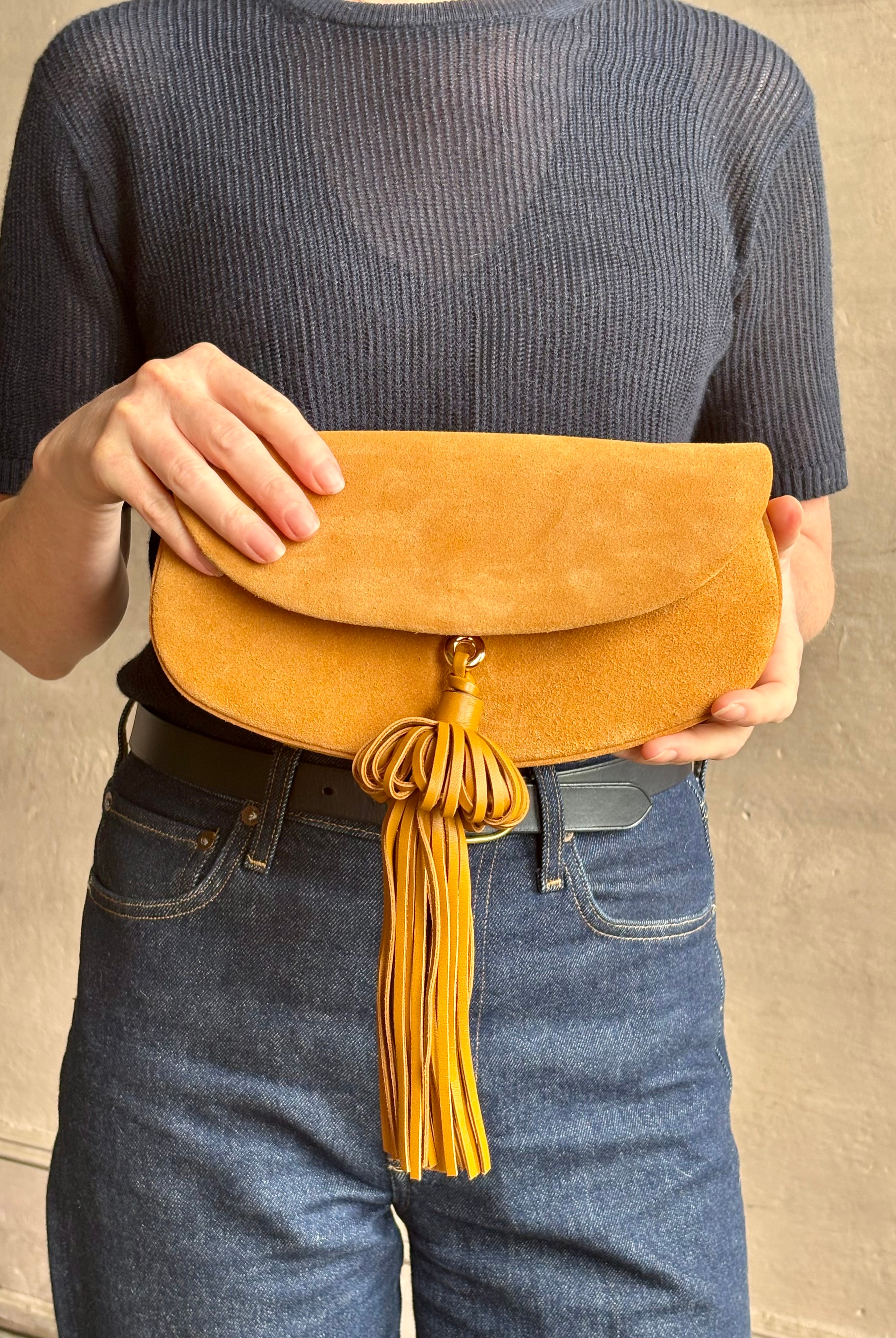 Mature woman with the luxury Italian leather Paloma handbag with Tassel Flap from Ulla Johnson rendered in a rich caramel brown featuring a pull tassel magnetic snap closure and removable adjustable handle that seamlessly converts to a designer clutch
