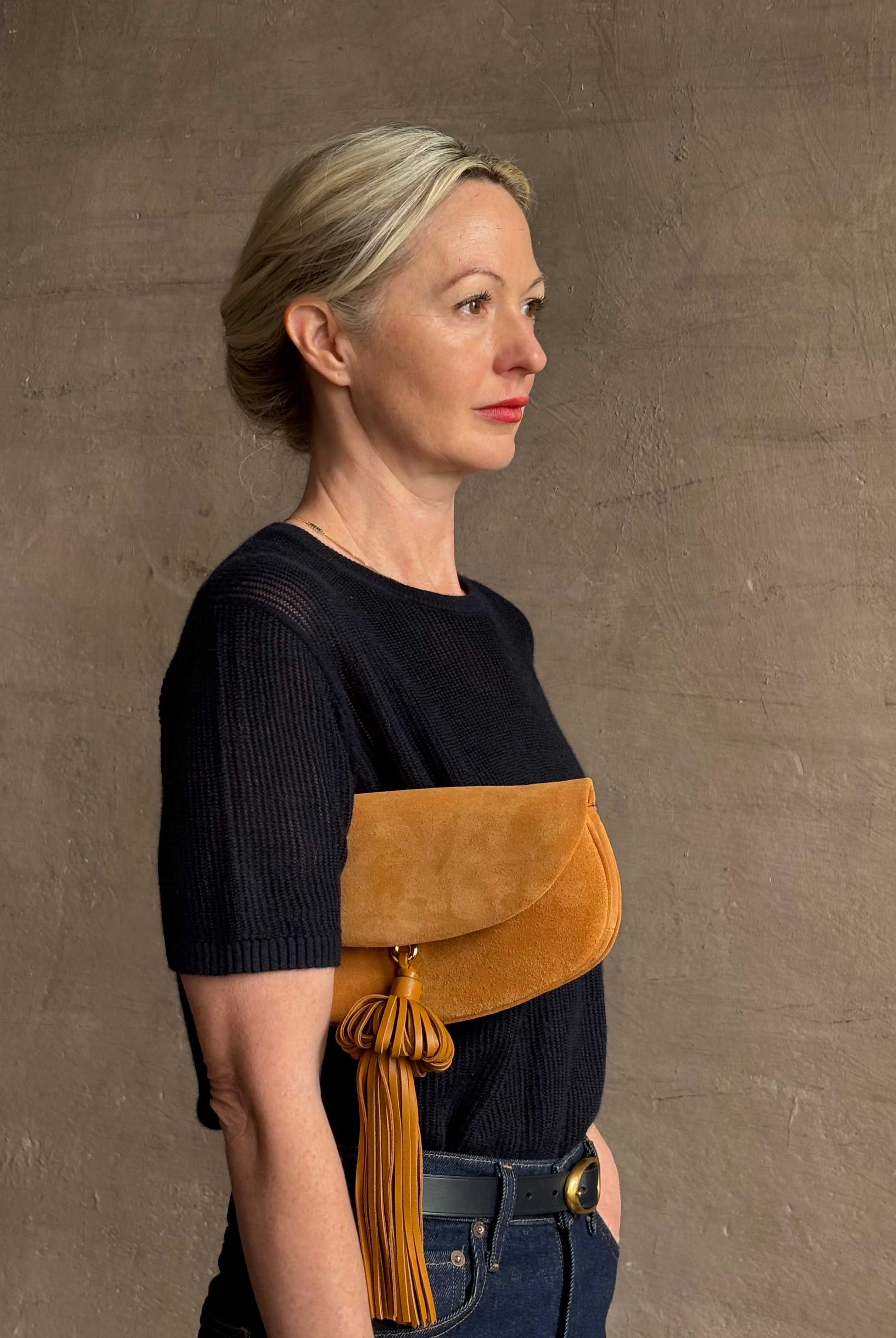 Mature woman with the luxury Italian leather Paloma handbag with Tassel Flap from Ulla Johnson rendered in a rich caramel brown featuring a pull tassel magnetic snap closure and removable adjustable handle that seamlessly converts to a designer clutch